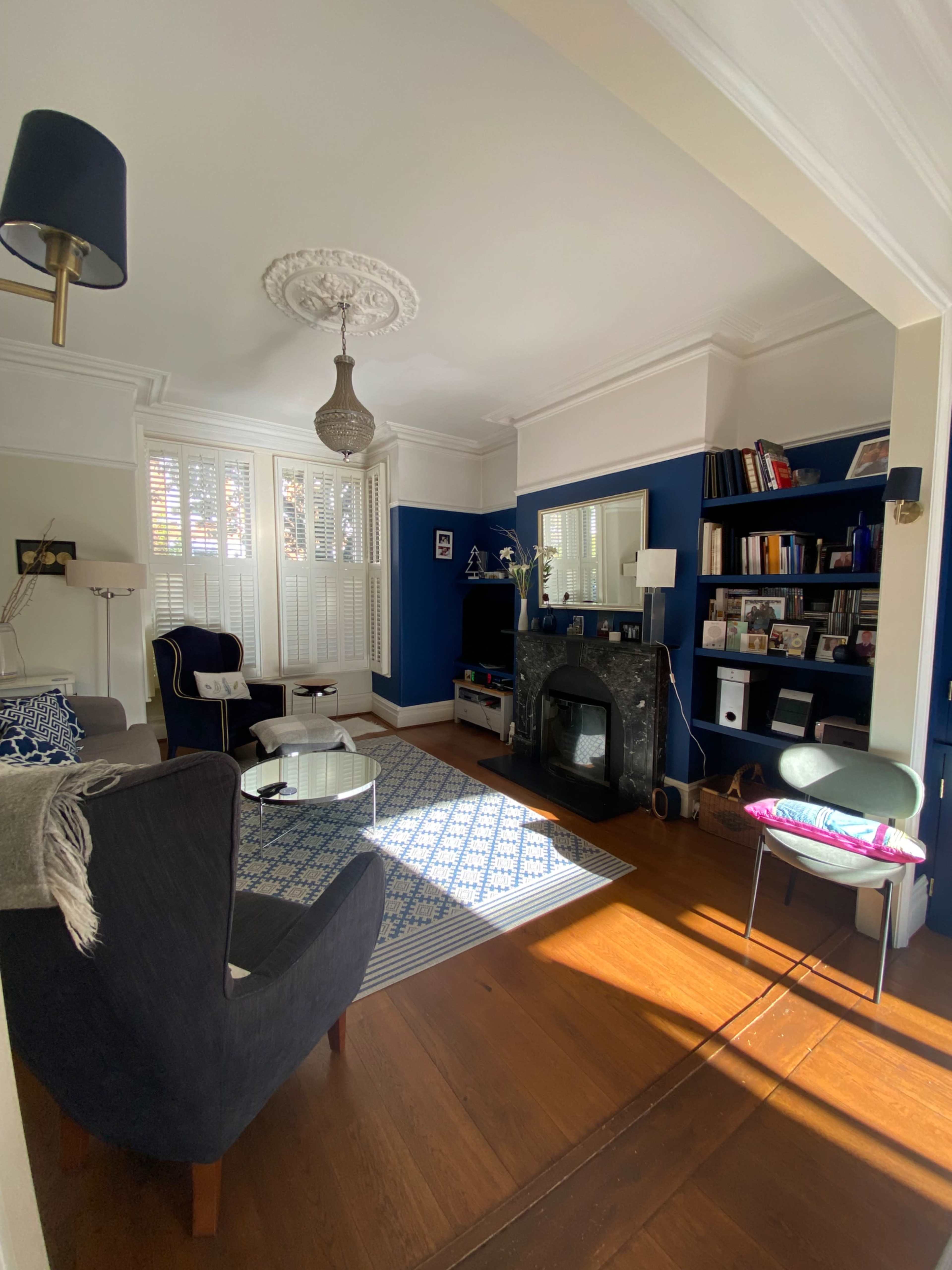 The living room features a dark blue accent wall, a fireplace, and a bookshelf filled with various items, illuminated by natural light.