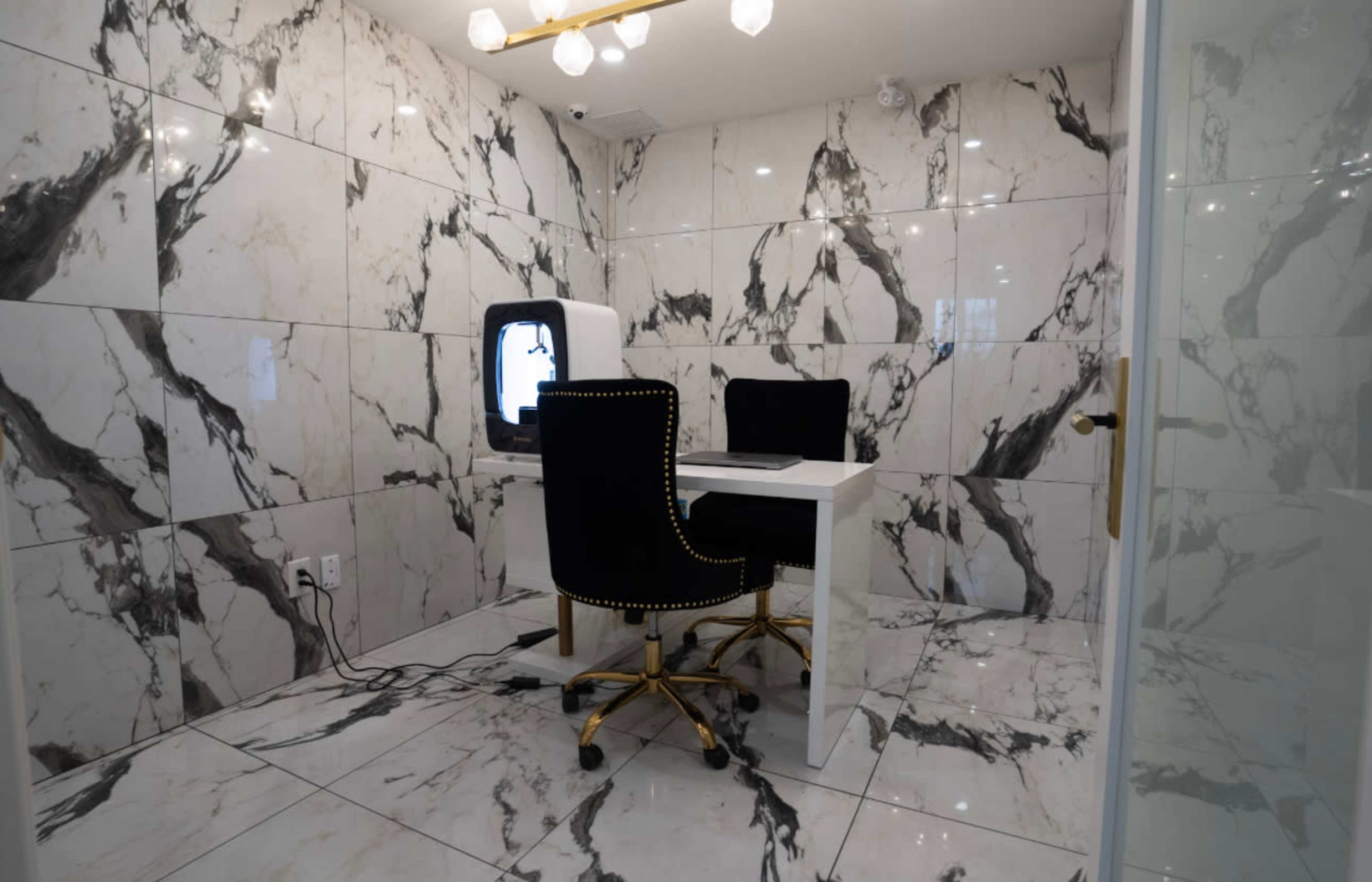 A small room with marble-patterned walls and flooring, featuring a white table and two black chairs with gold accents.