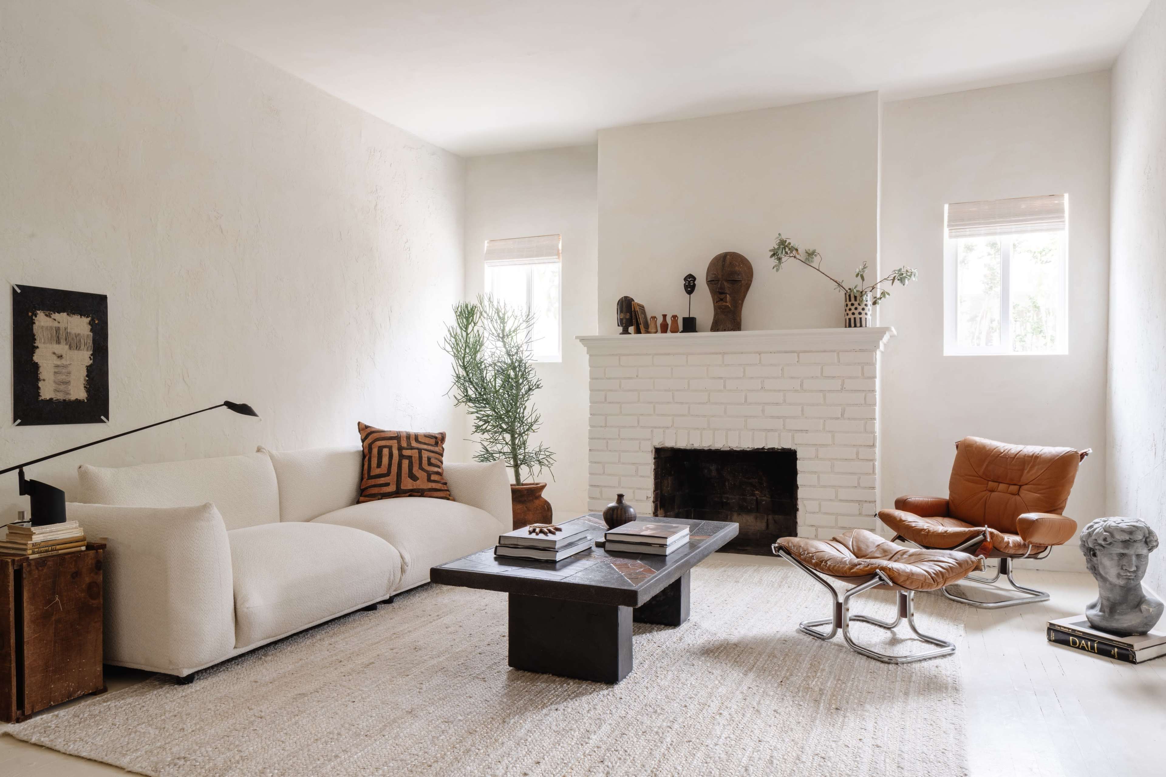 A minimalist living room with a white sofa, a dark wooden coffee table, and a fireplace with decorative objects on the mantel.