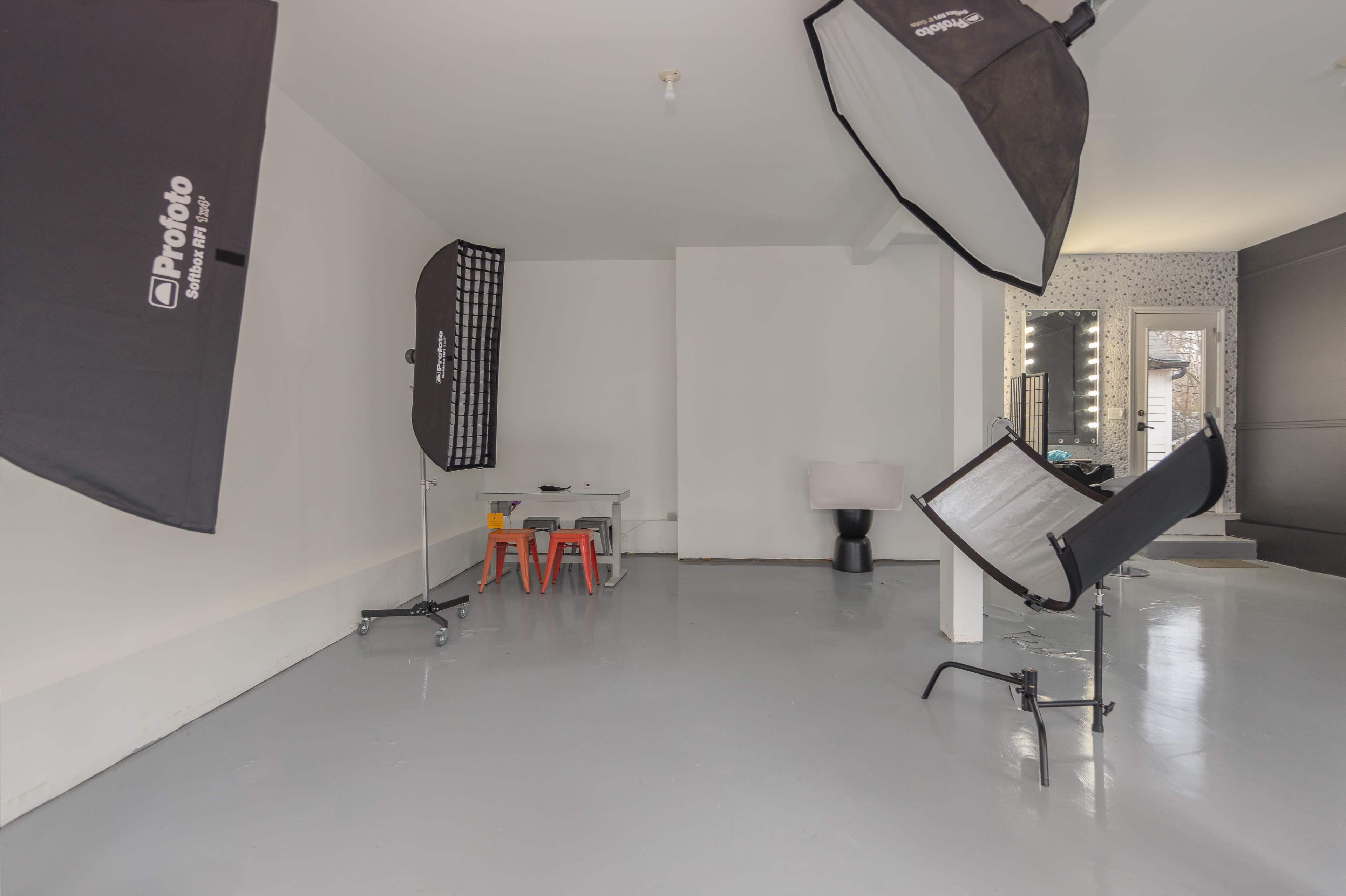 A minimal studio space equipped with photography lighting setups, a small table with chairs, and a lamp in the corner.