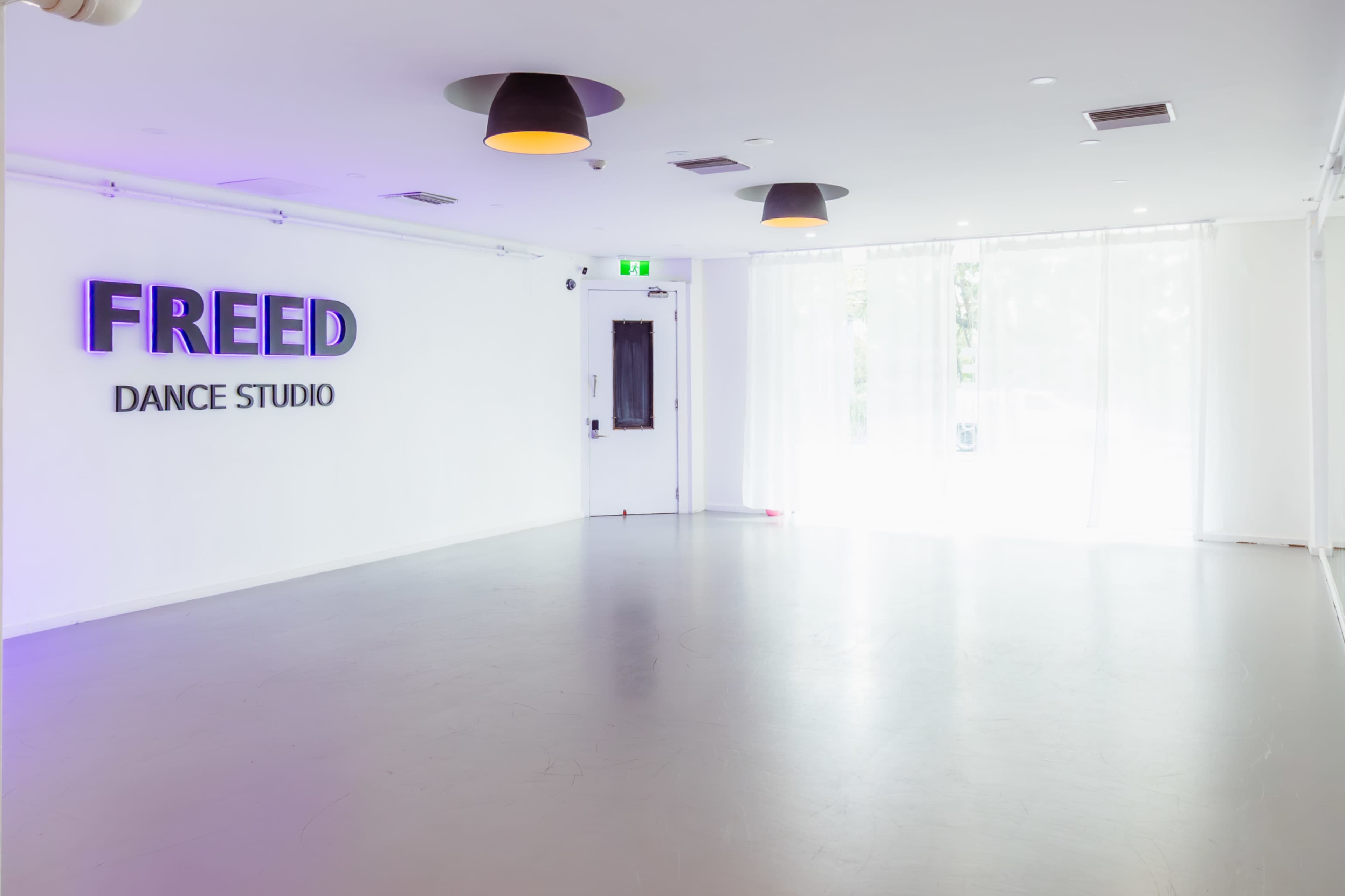 The image shows an interior of a dance studio featuring a large sign that reads "FREED DANCE STUDIO" on a white wall, with bright lighting and a spacious, uncluttered floor.