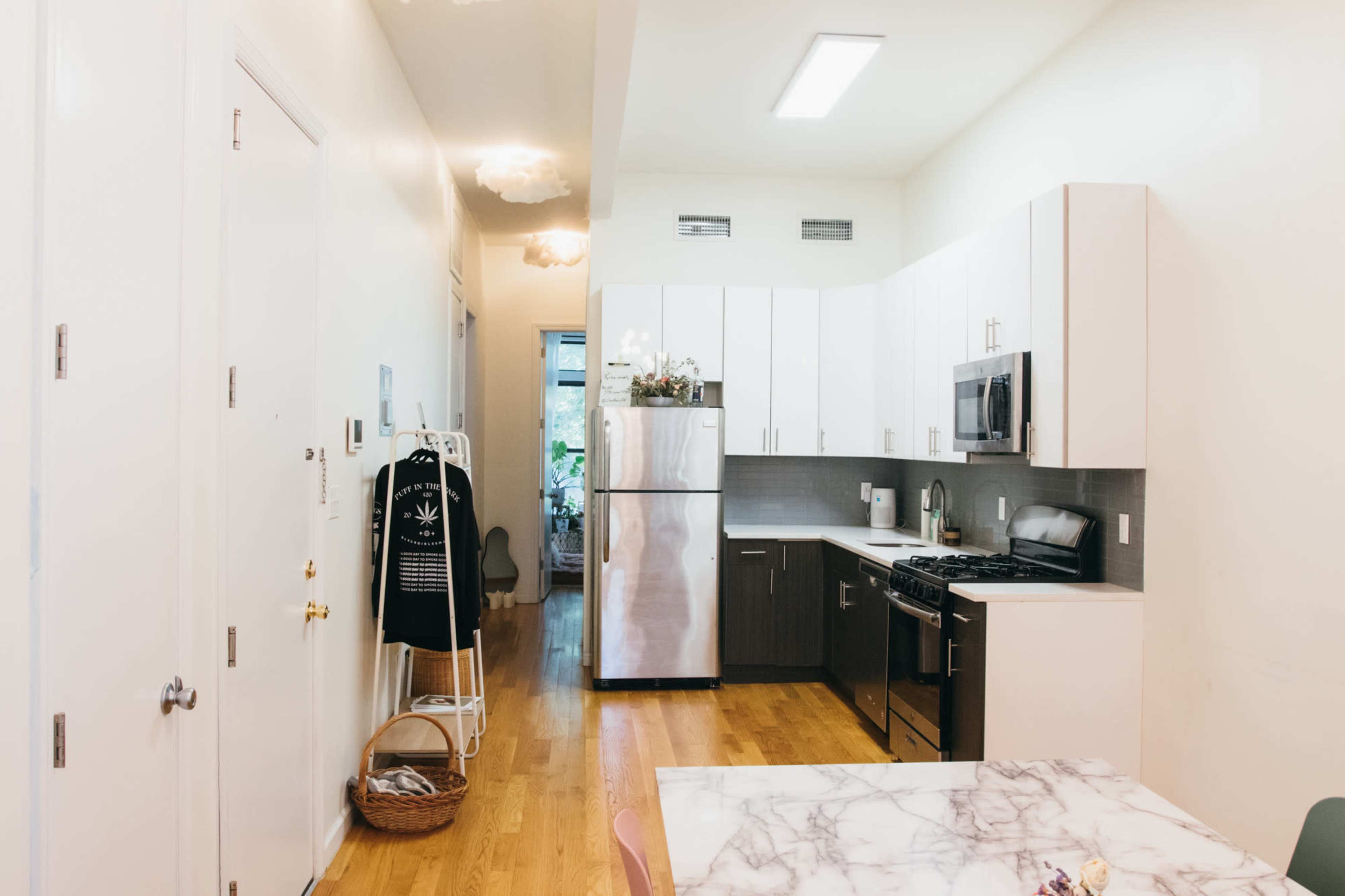 A modern kitchen with white cabinetry, stainless steel appliances, and a marble dining table in a well-lit space.