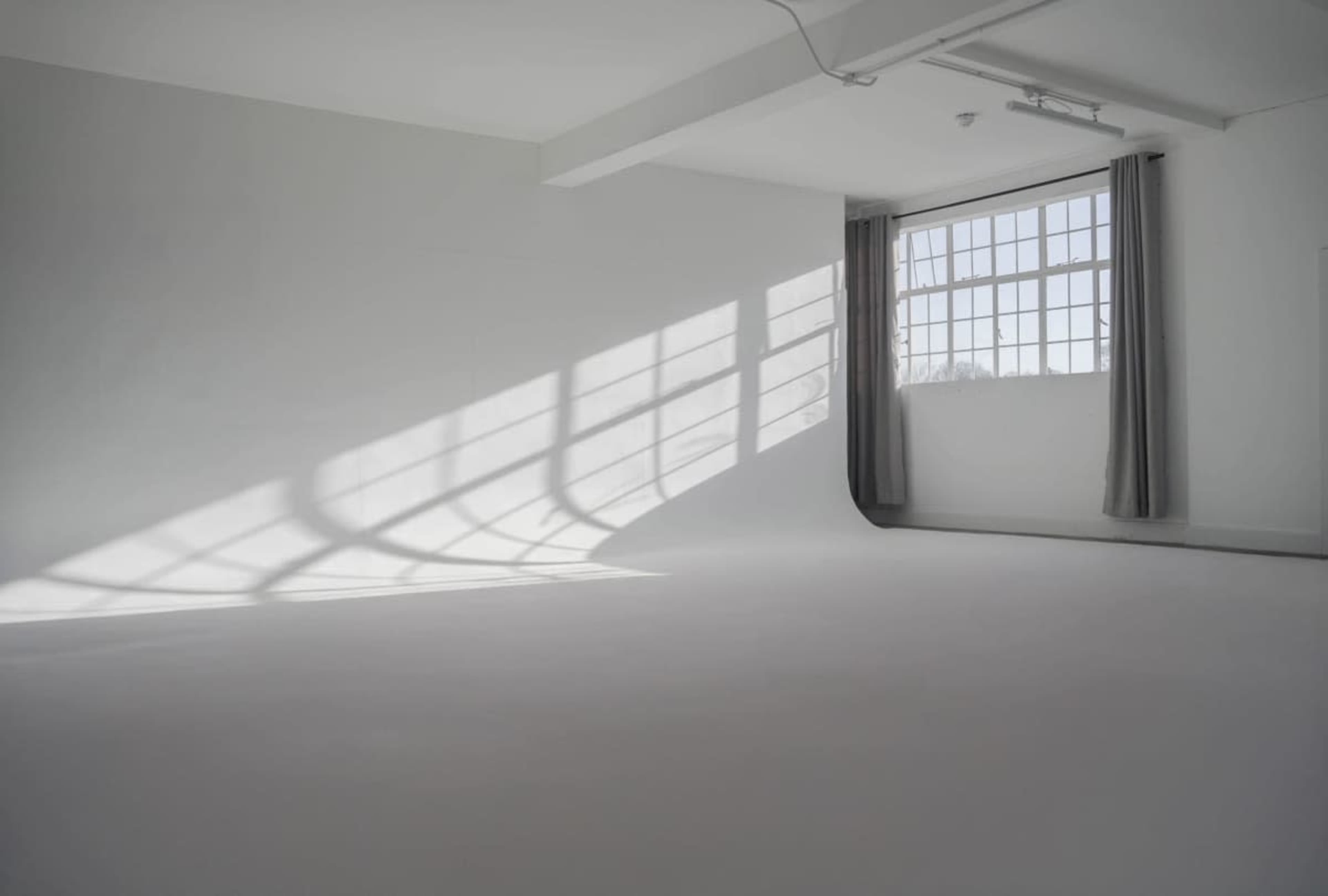 A bright, empty room with white walls and a large window casting shadows on the floor.