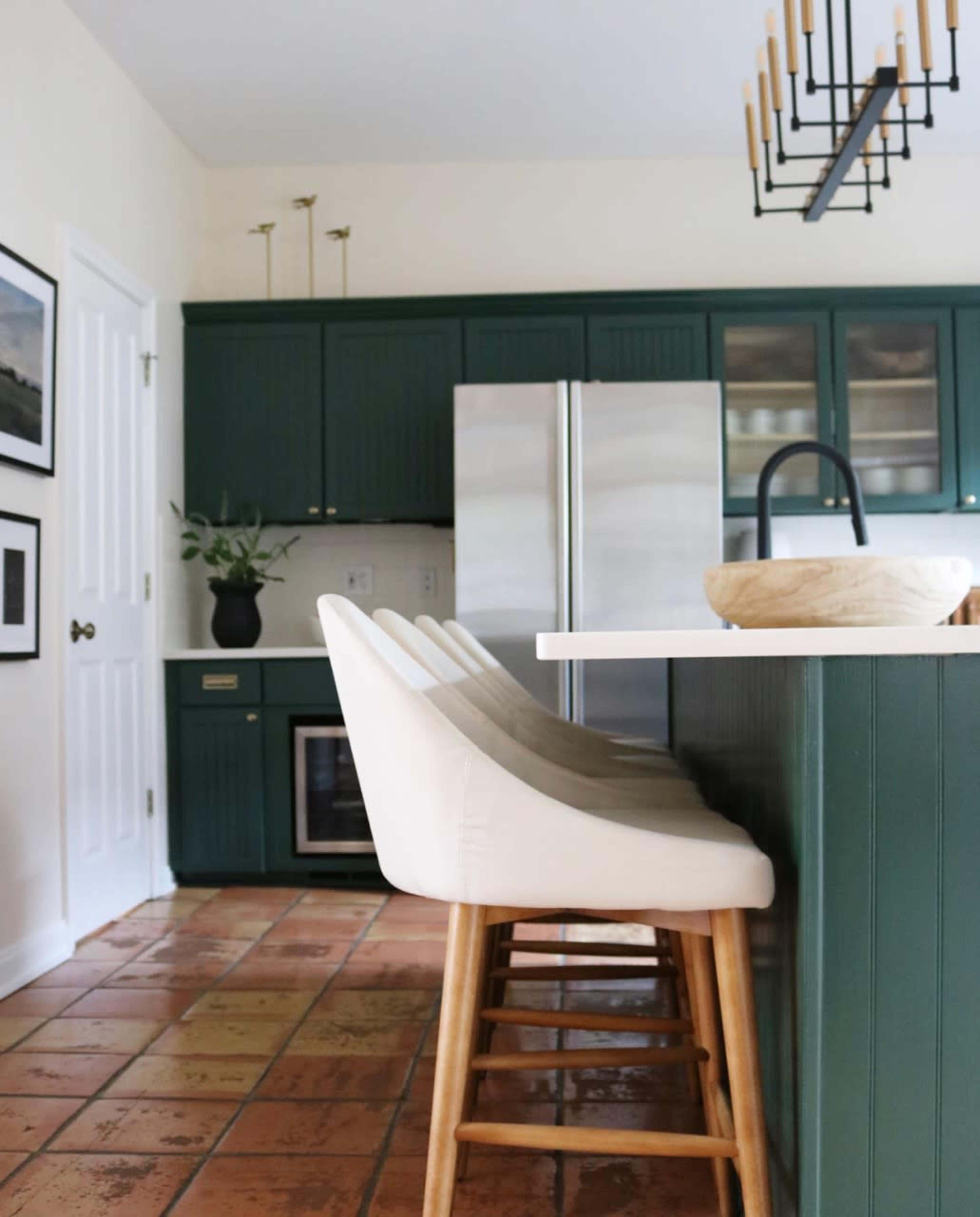 A kitchen features green cabinetry, a large island with white bar stools, and stainless steel appliances.