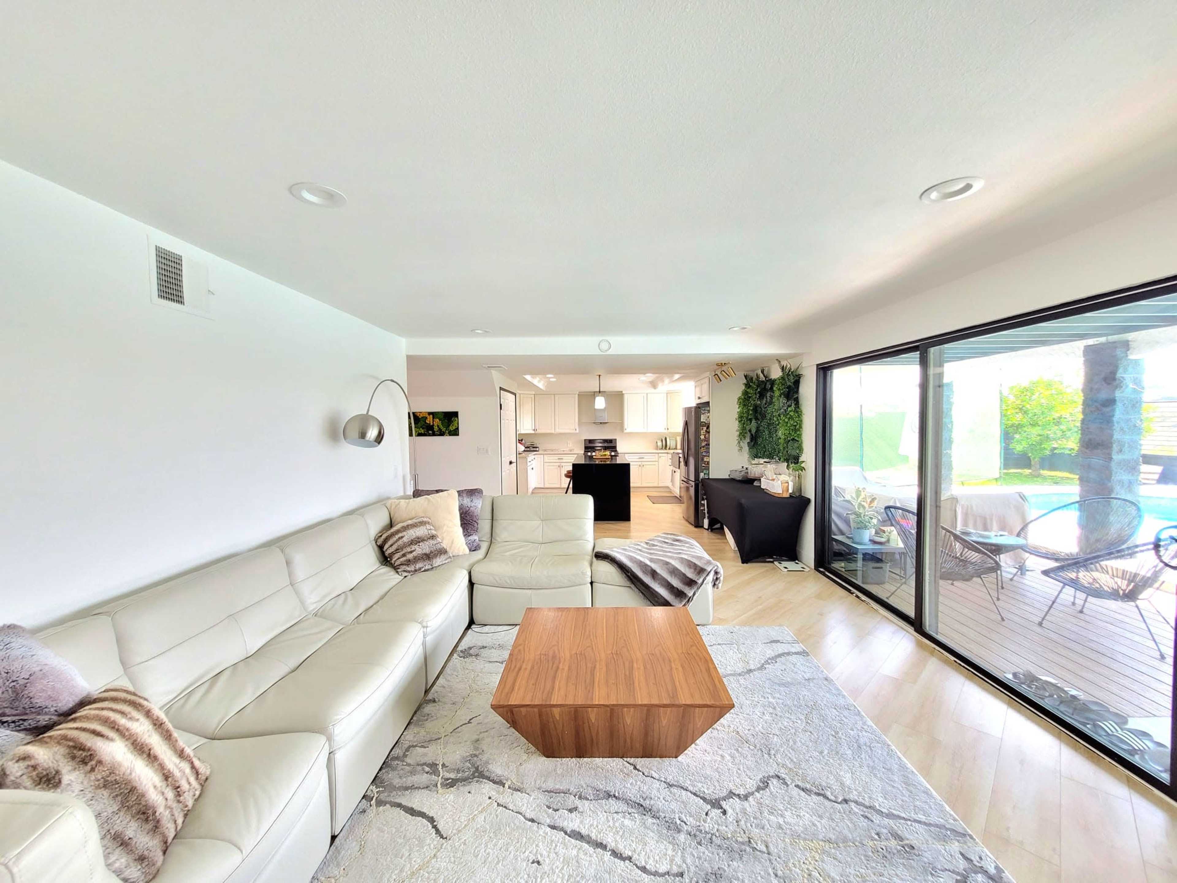 A modern living room with a light-colored sectional sofa, a wooden coffee table, and large glass doors leading to an outdoor space with a pool.