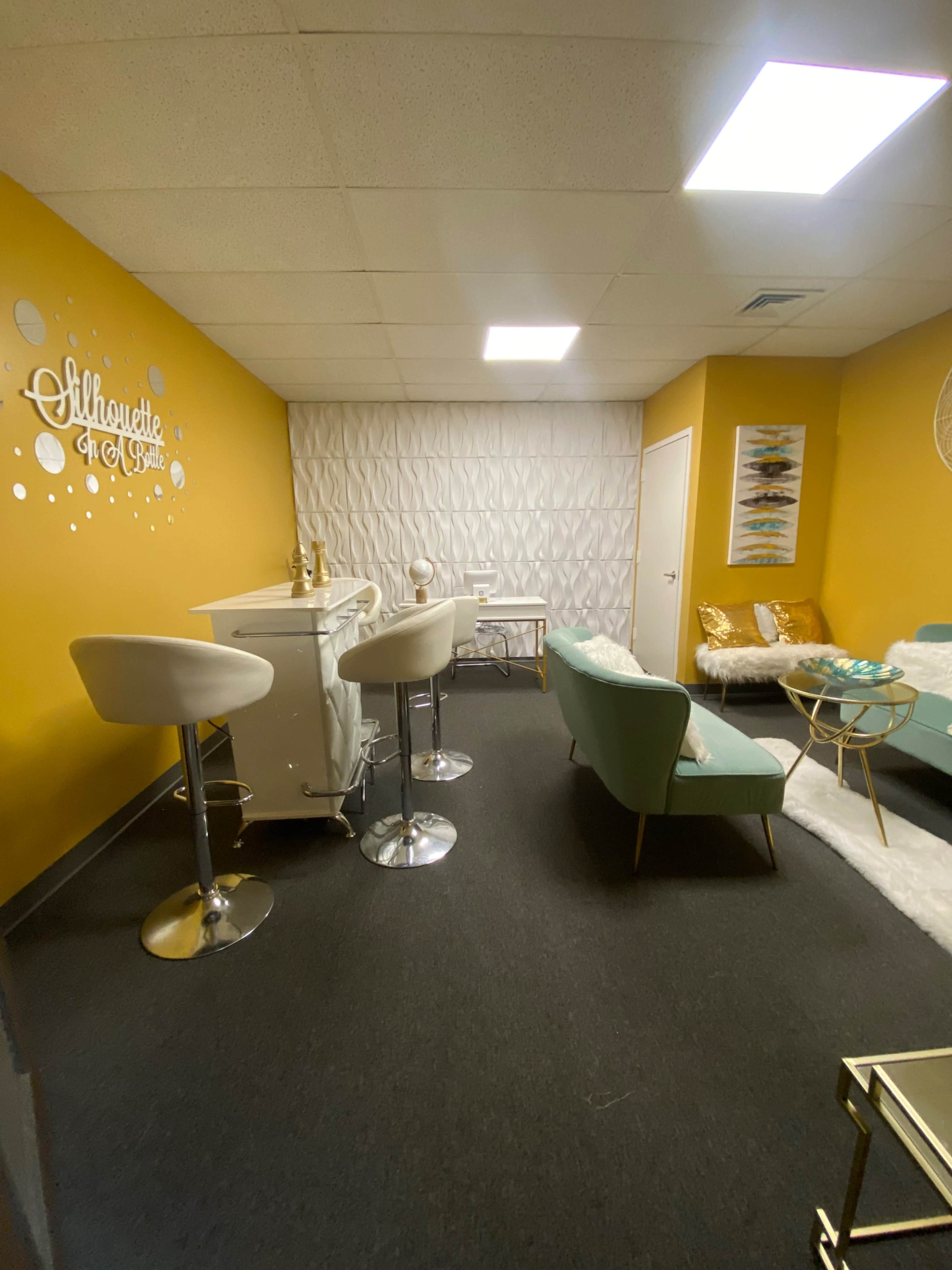 A small lounge area with teal furniture, a bar cart, and yellow walls, featuring decorative accents like a wall with circular designs and a textured white panel.