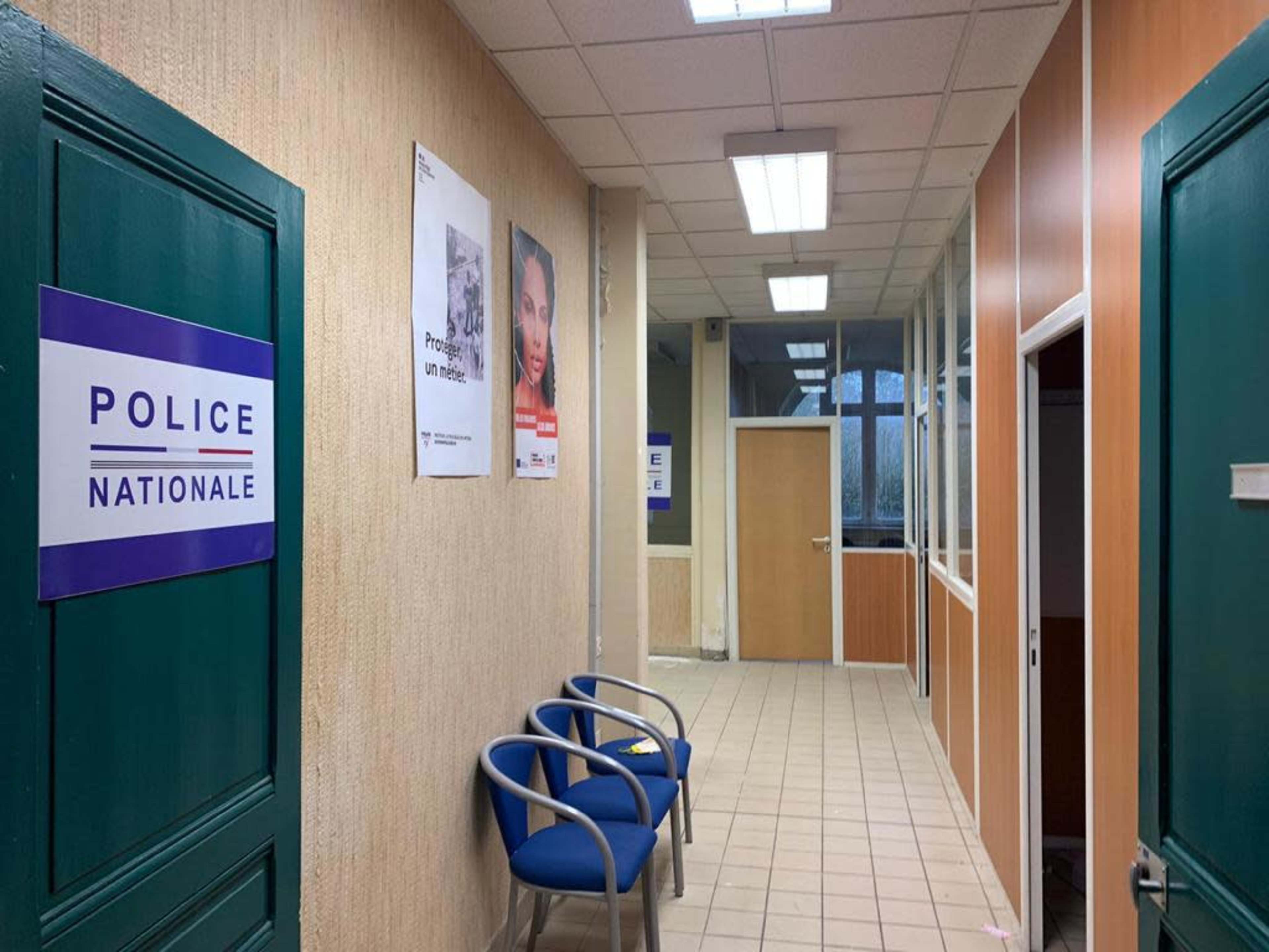 A hallway in a police station with blue chairs, signs for "Police Nationale," and posters on the walls.