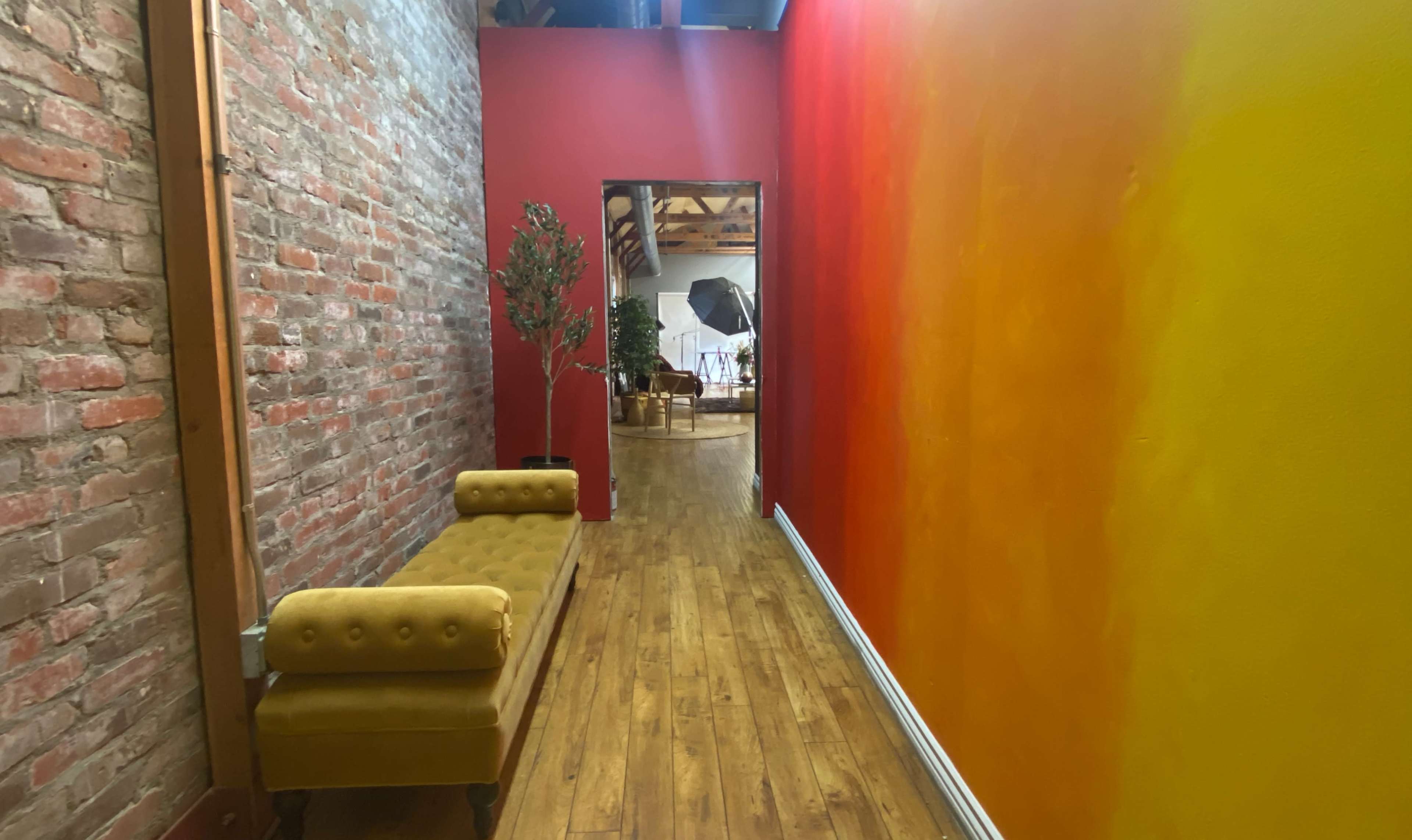 A narrow hallway features a brick wall on one side and a gradient orange wall on the other, with a yellow bench along the brick side.
