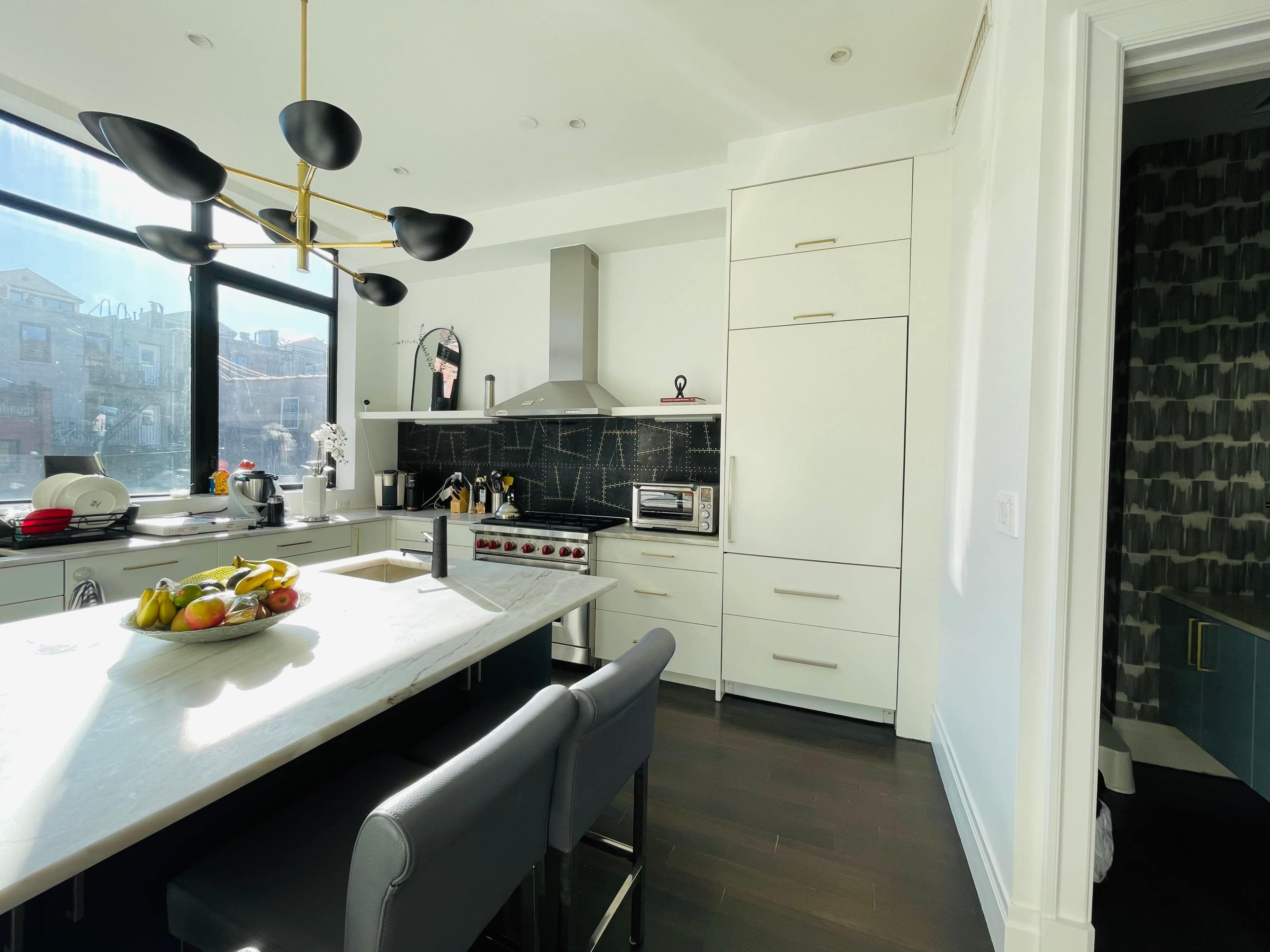 A modern kitchen featuring a central island with a fruit bowl, a sleek stove, and white cabinetry against a black tiled backsplash.