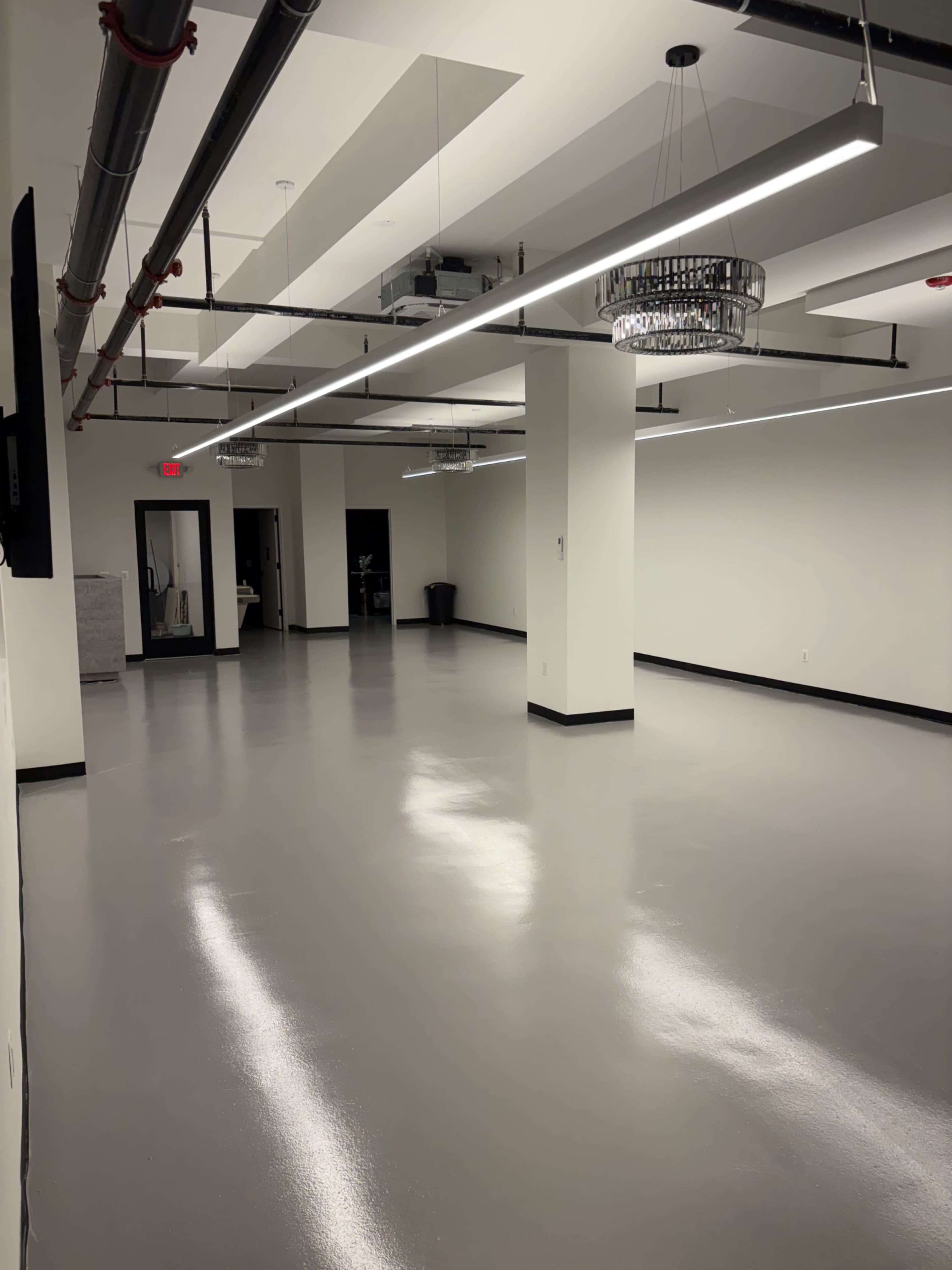 The image shows a spacious, empty room with polished gray flooring, white walls, and overhead lighting fixtures.