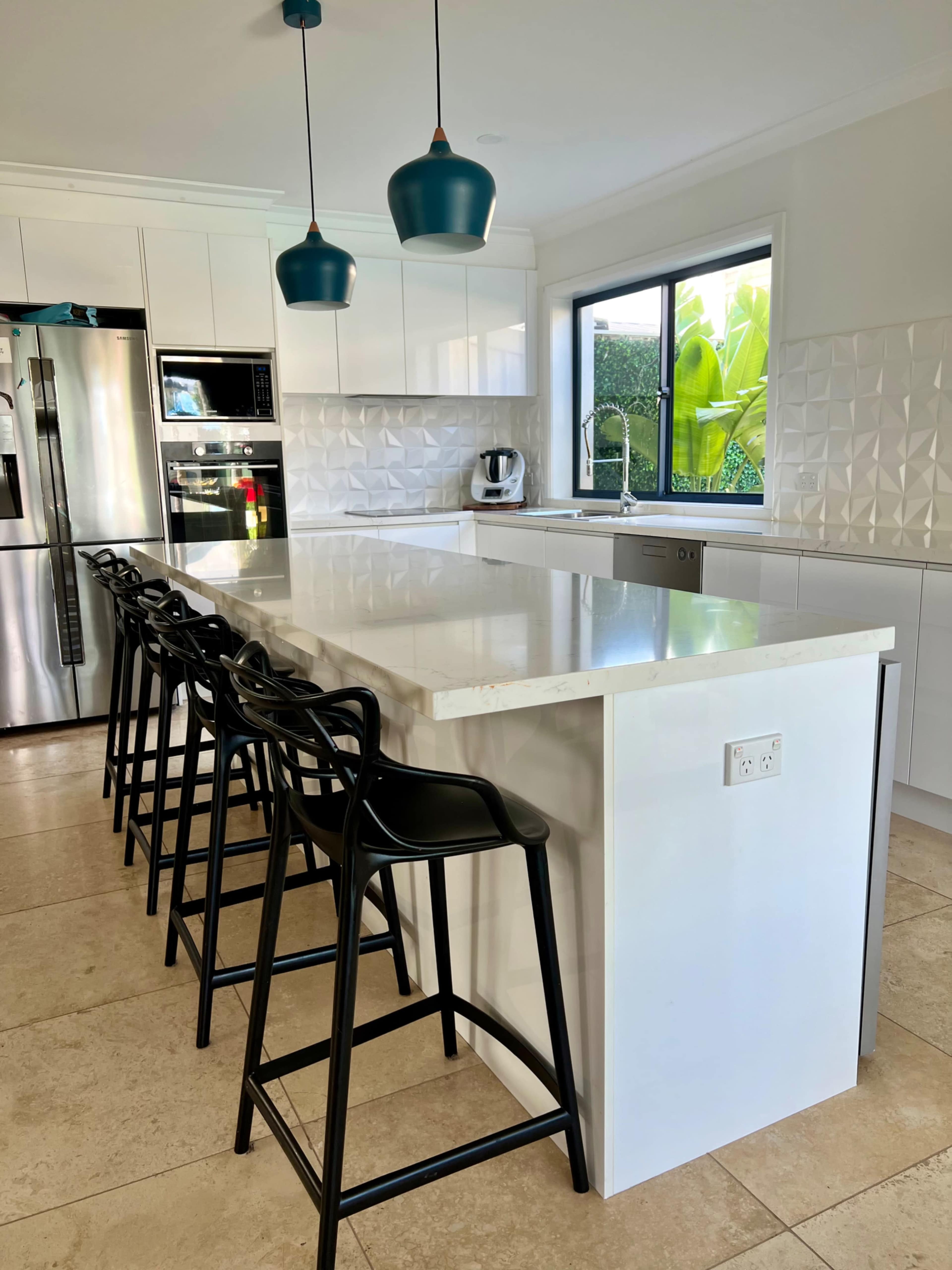 The image shows a modern kitchen with a large white island, black bar stools, and pendant lights above.