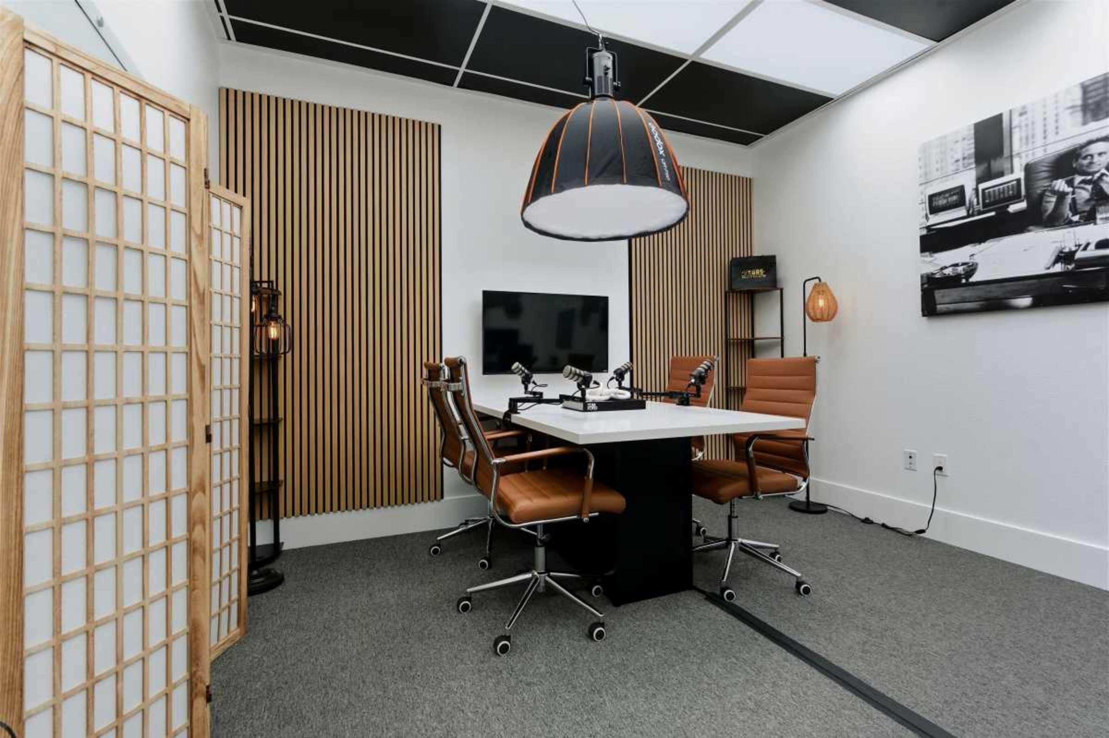 A modern conference room features wooden accent walls, a central white table with four leather chairs, and contemporary lighting fixtures.