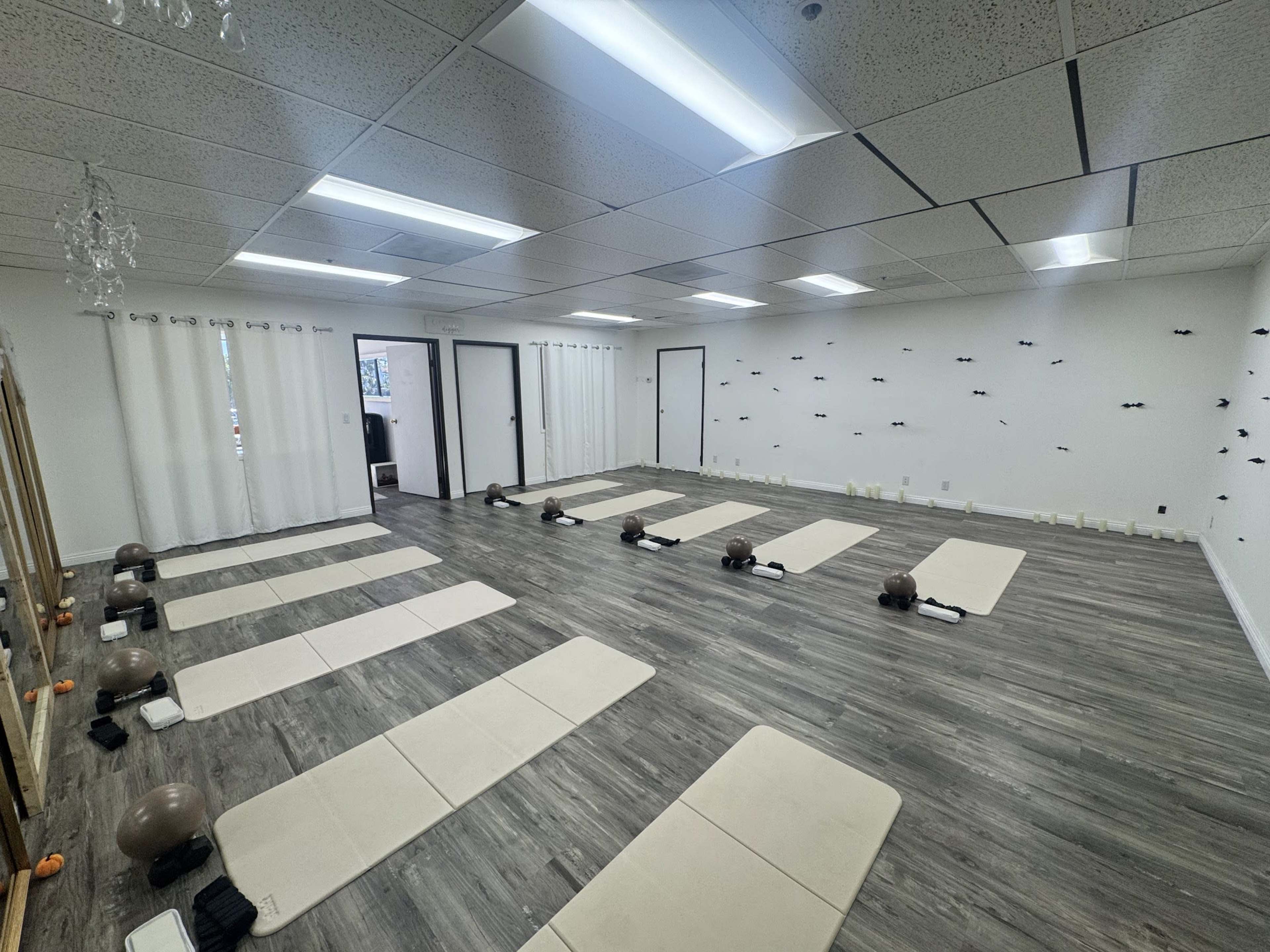 The image shows a spacious, uncluttered yoga studio featuring several exercise mats arranged in rows, with mirrors and soft lighting illuminating the area.