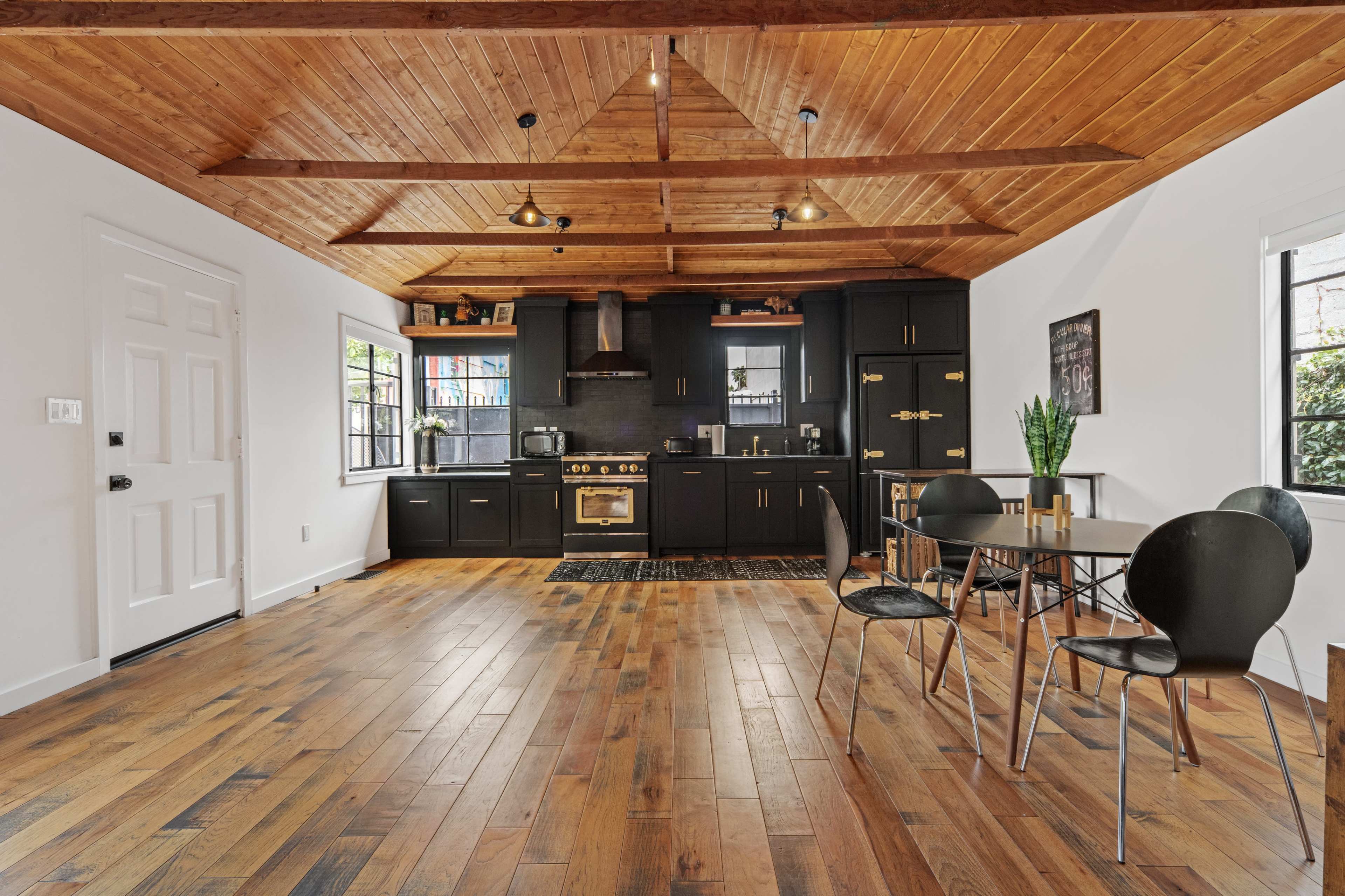 A modern kitchen with black cabinetry and wooden ceilings, featuring a dining table and chairs arranged in the foreground.