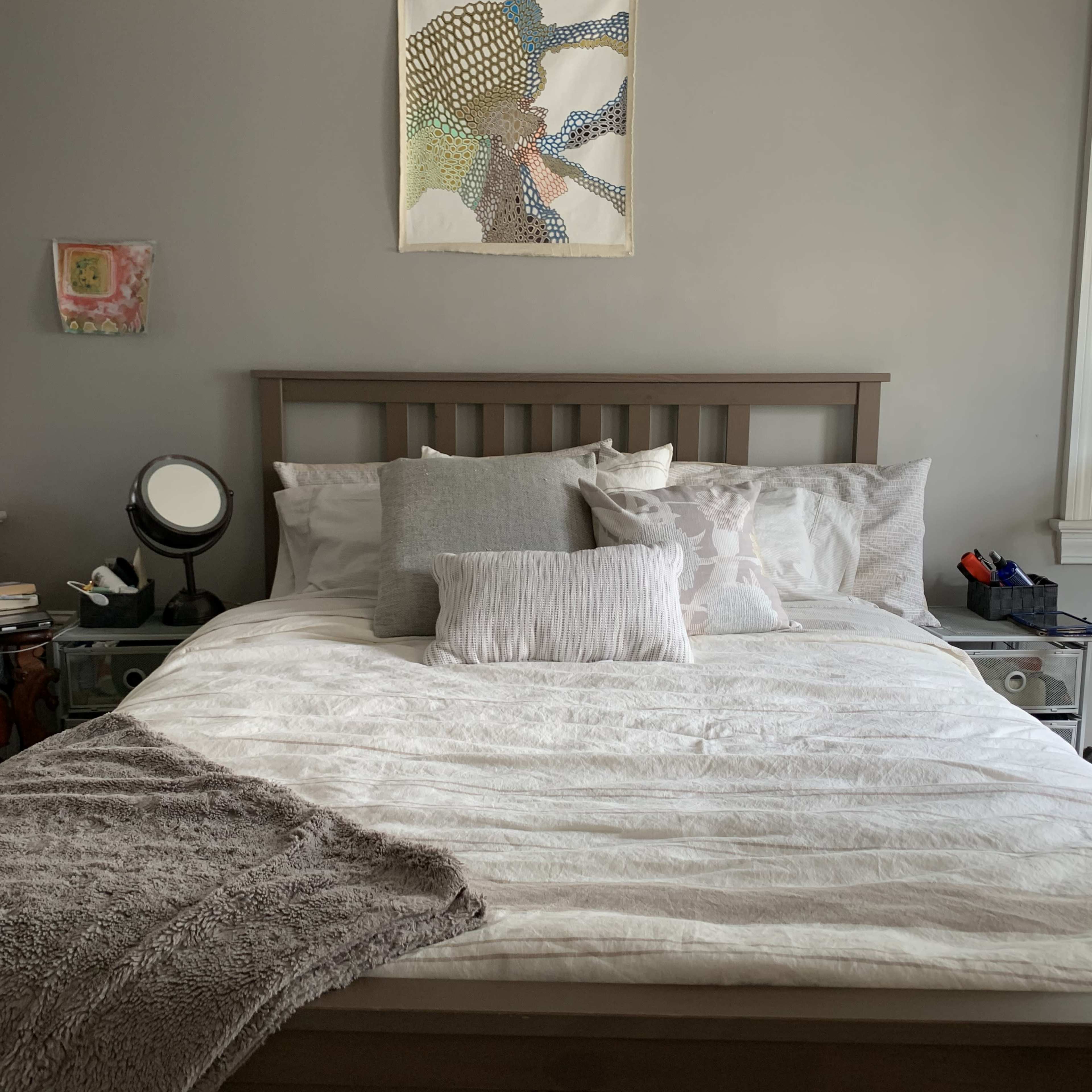 A neatly made bed with an assortment of pillows is positioned against a gray wall in a well-lit bedroom.