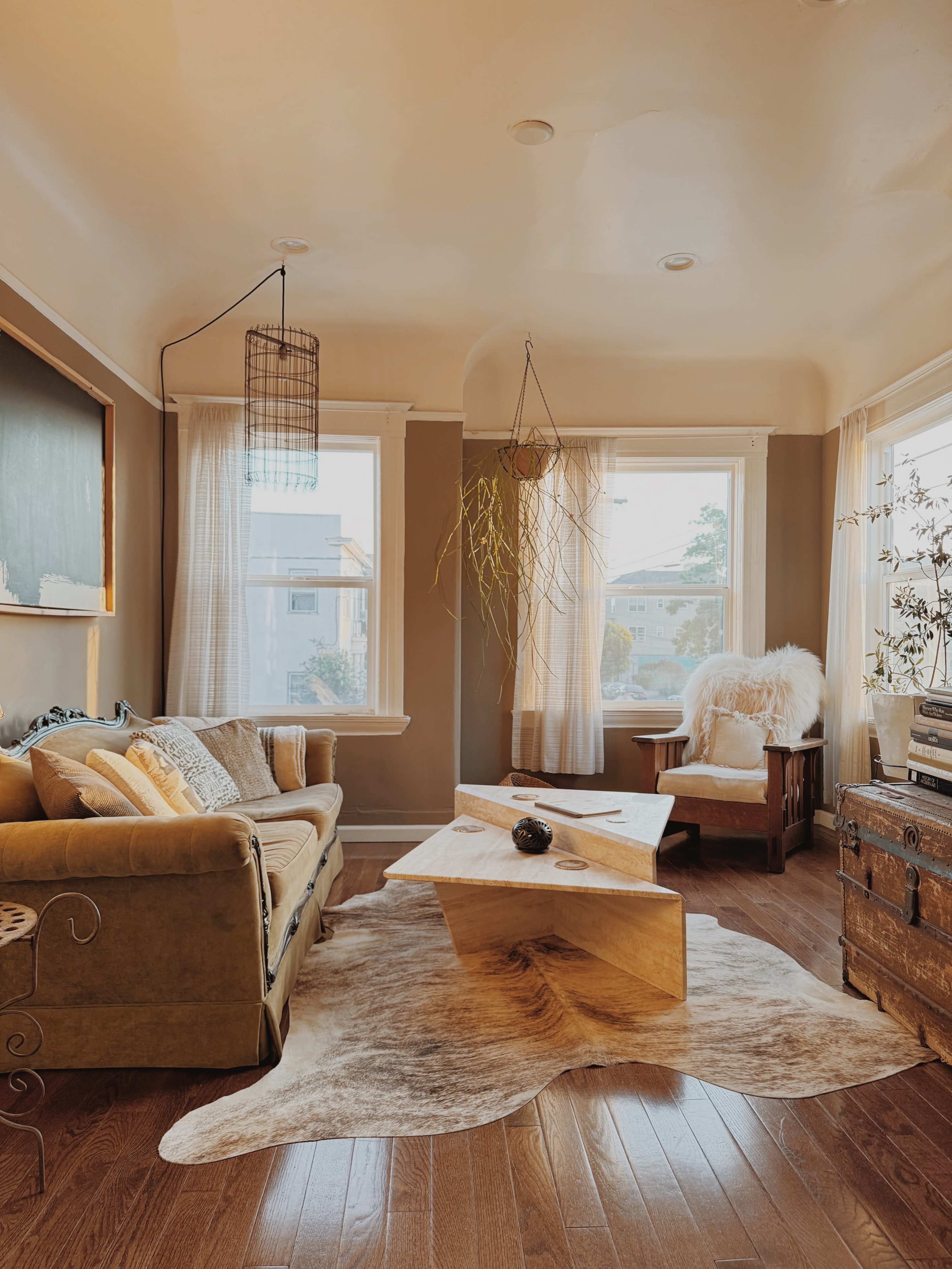 The image shows a cozy living room with a green couch, a wooden coffee table, and large windows allowing natural light to enter.