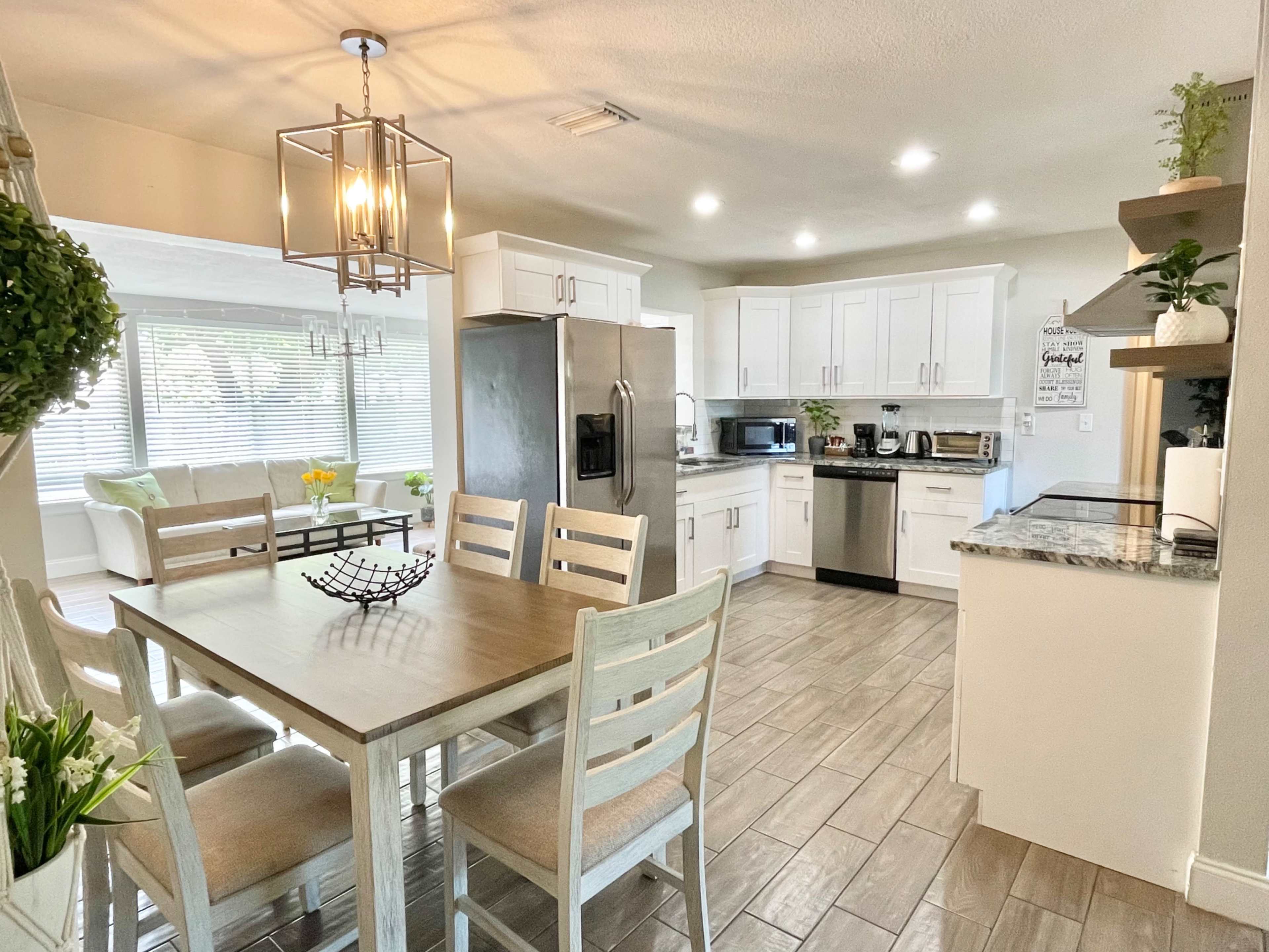 A modern kitchen with white cabinets, stainless steel appliances, and a dining table set for four, illuminated by a hanging light fixture.