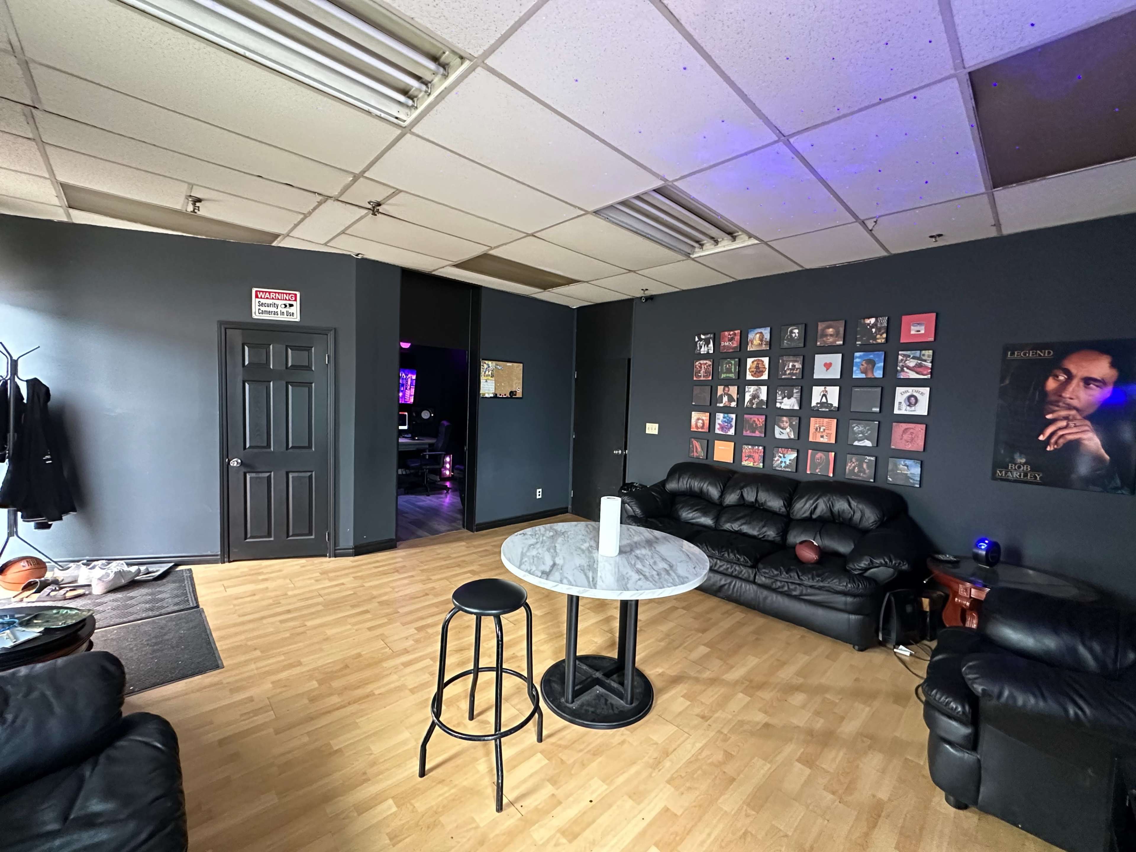 The image shows a lounge area with black leather couches, a marble-top table, and a wall featuring framed photographs and artwork.
