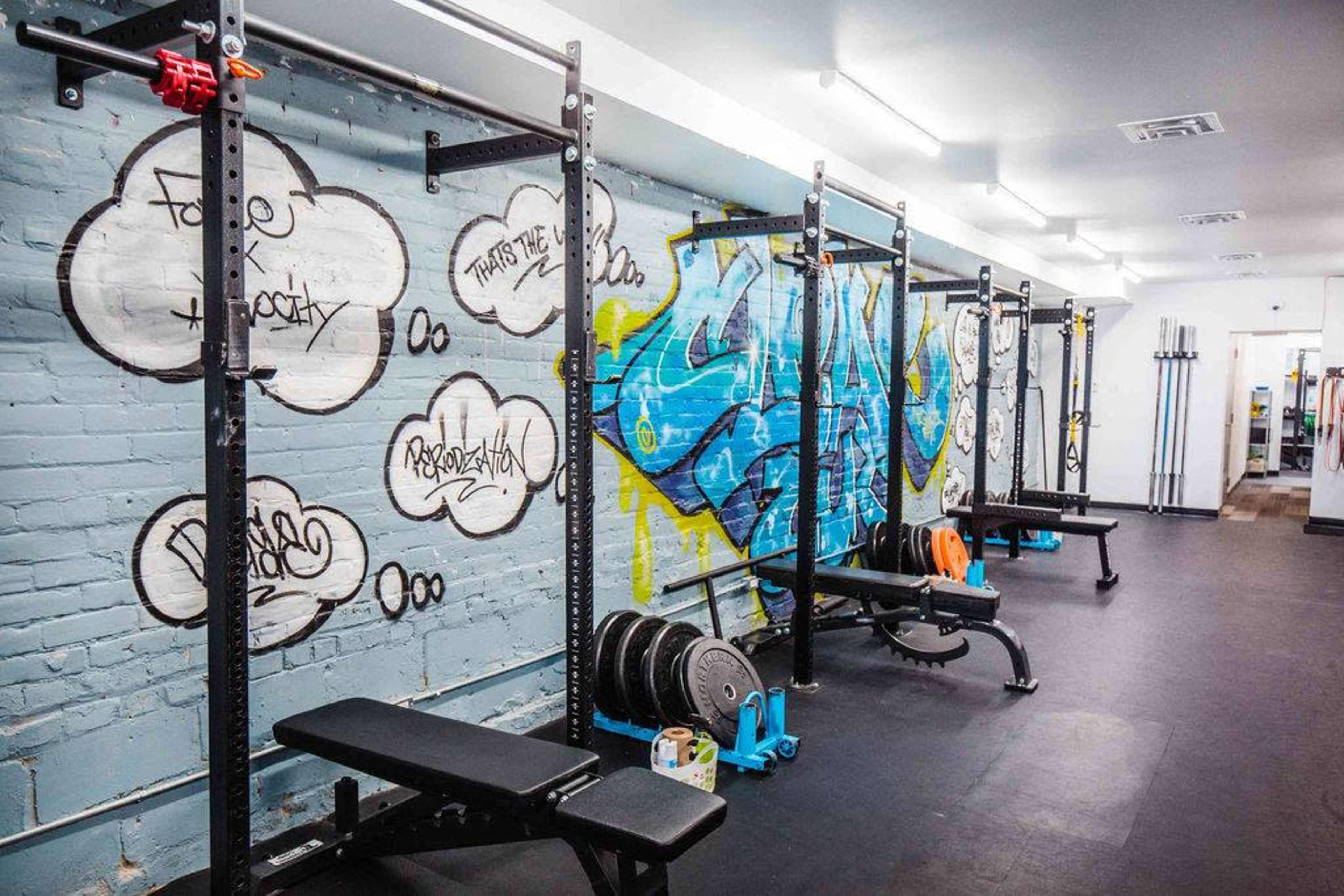 A gym interior with weightlifting equipment and colorful graffiti on the walls.
