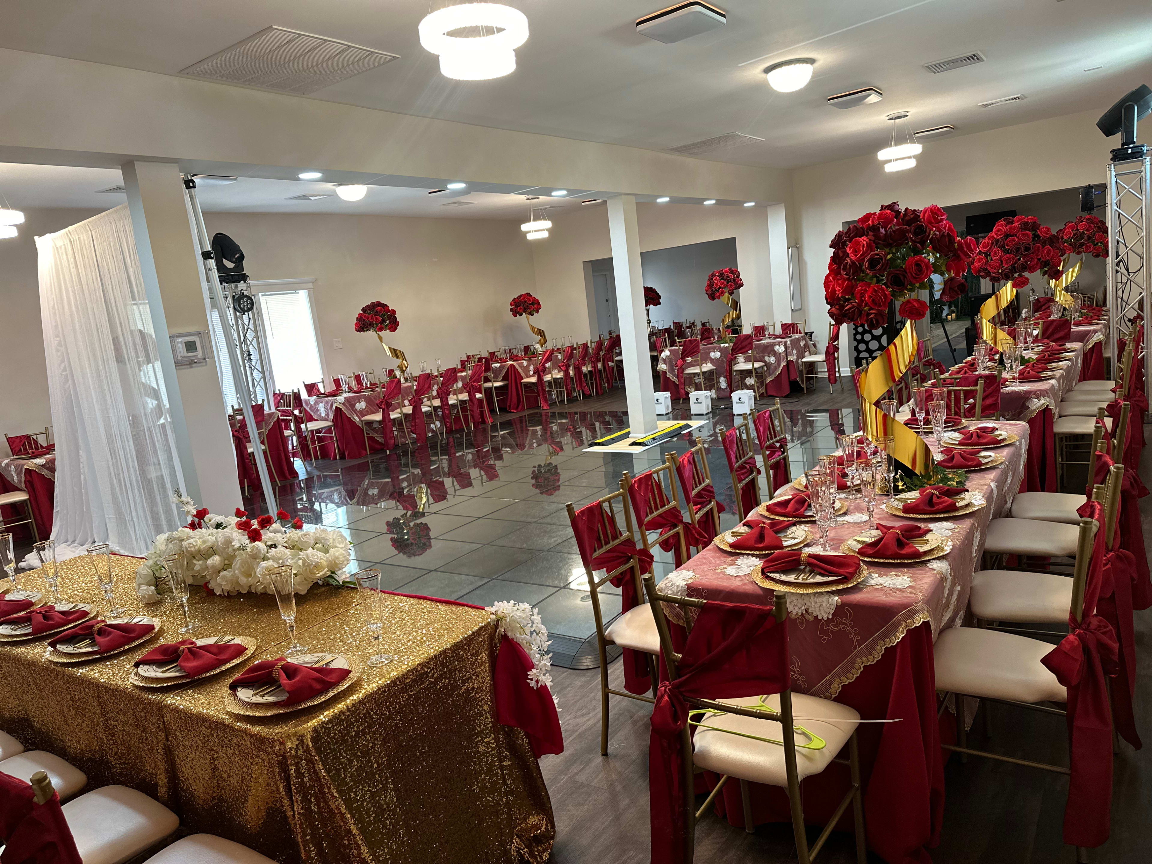 A banquet hall set up for an event, featuring red and gold tablecloths, floral centerpieces, and large floral arrangements.