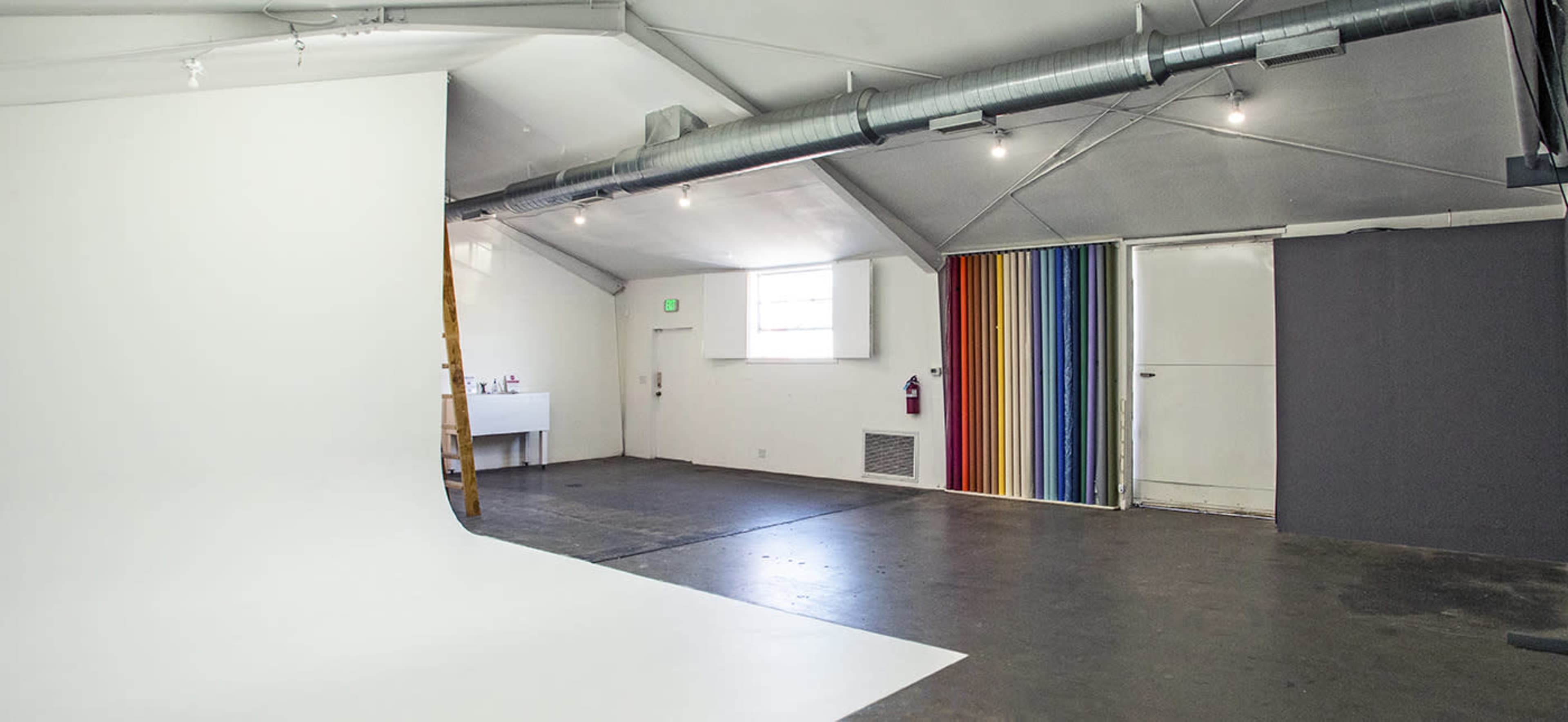 A spacious studio interior with a white backdrop, a wooden ladder, and colorful striped and gray walls.