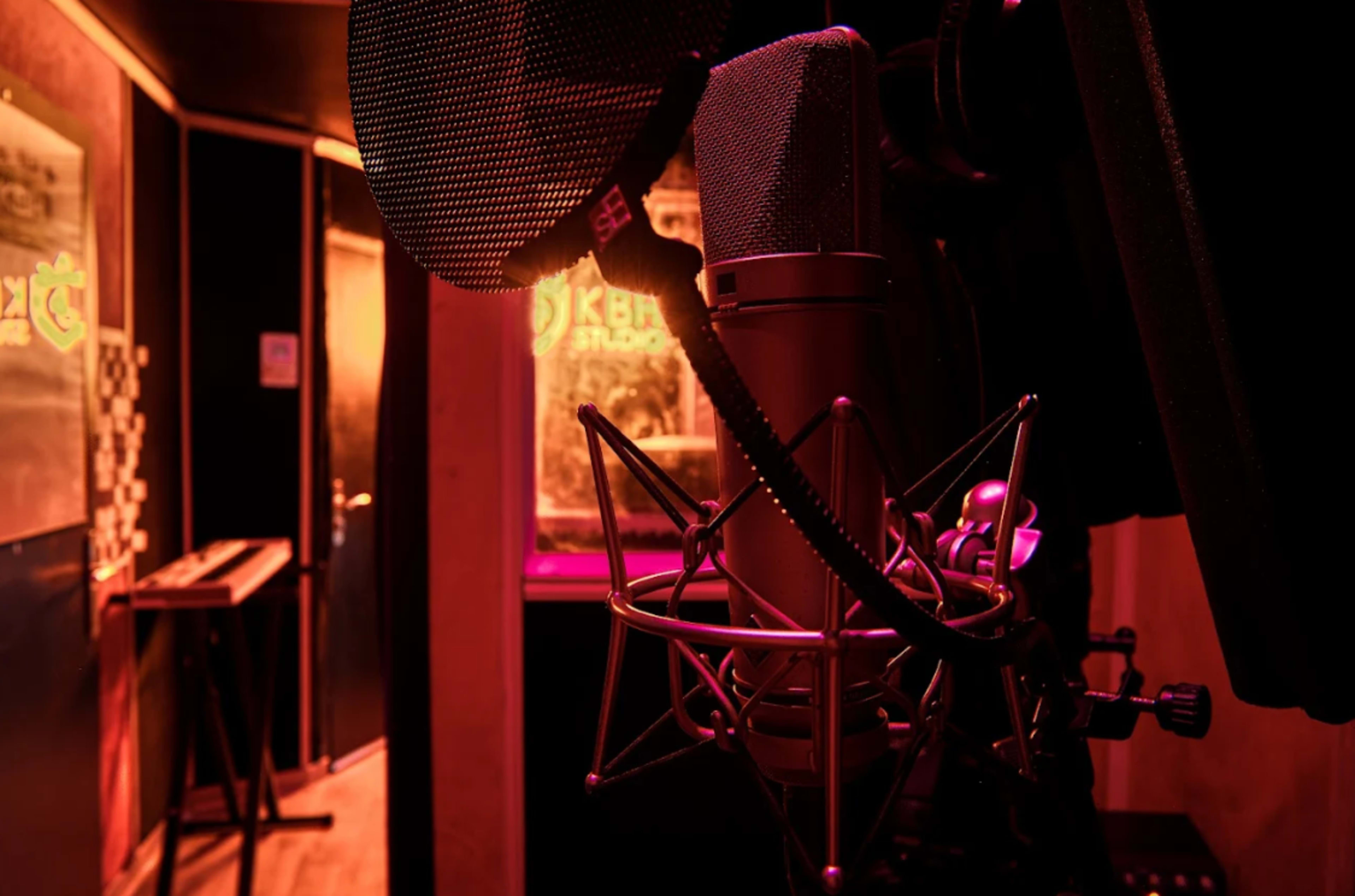 A close-up view of a microphone in a recording studio with dim purple lighting and a corridor in the background.