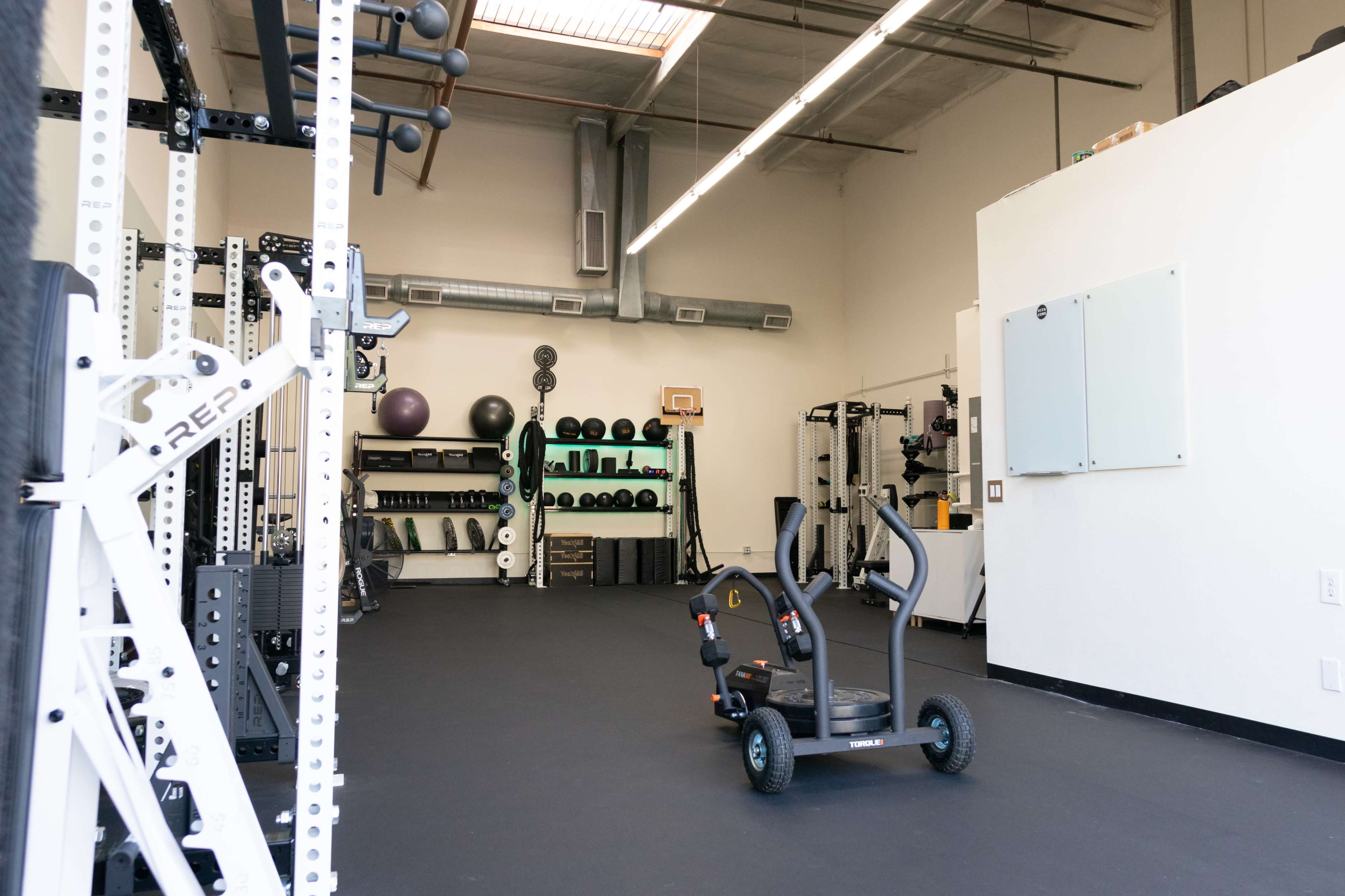 A spacious gym with workout equipment, a sled, and exercise accessories organized on shelves.