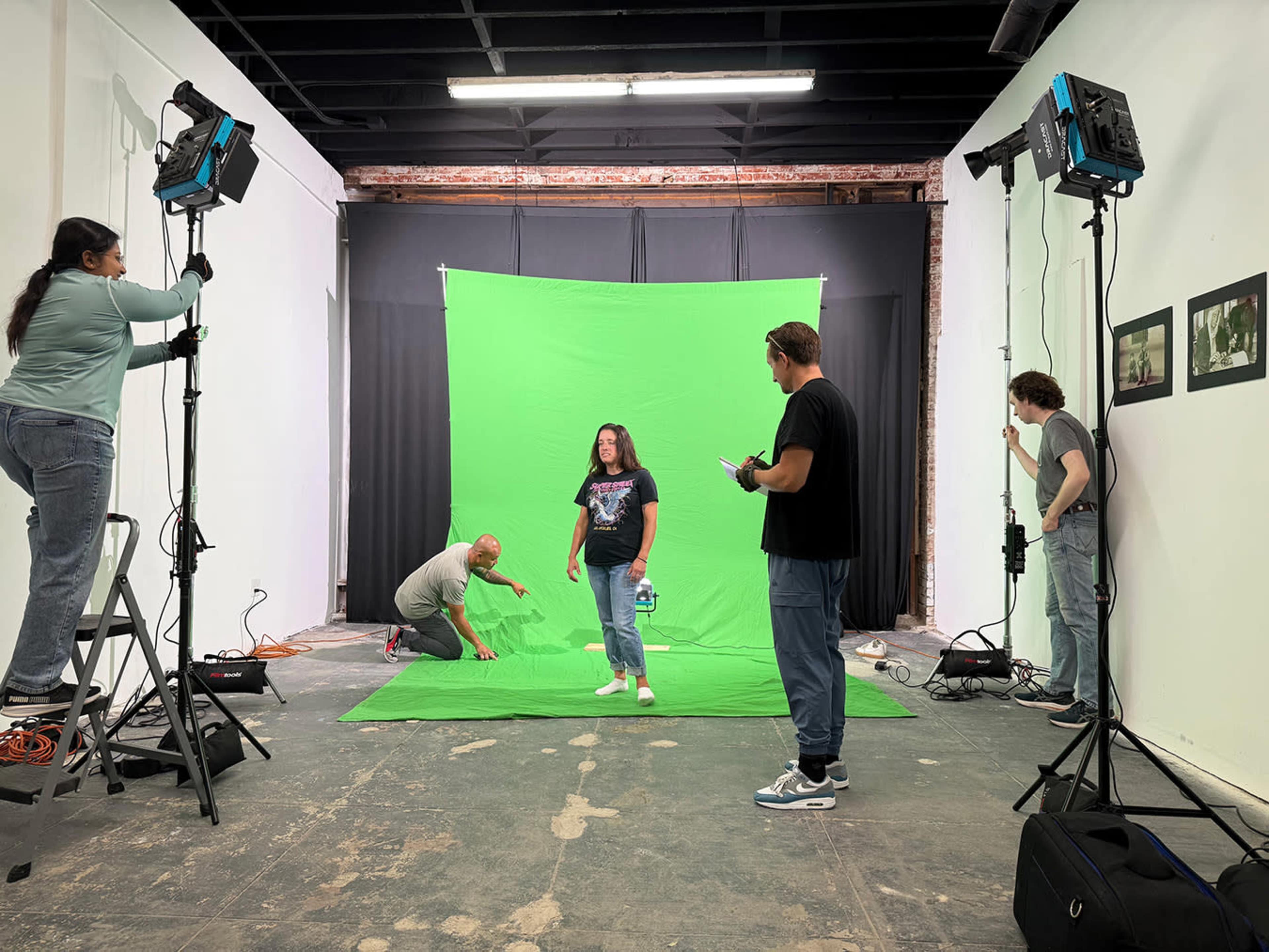 A group of five people is working in a studio with a green screen backdrop, setting up lighting and props for a photoshoot.