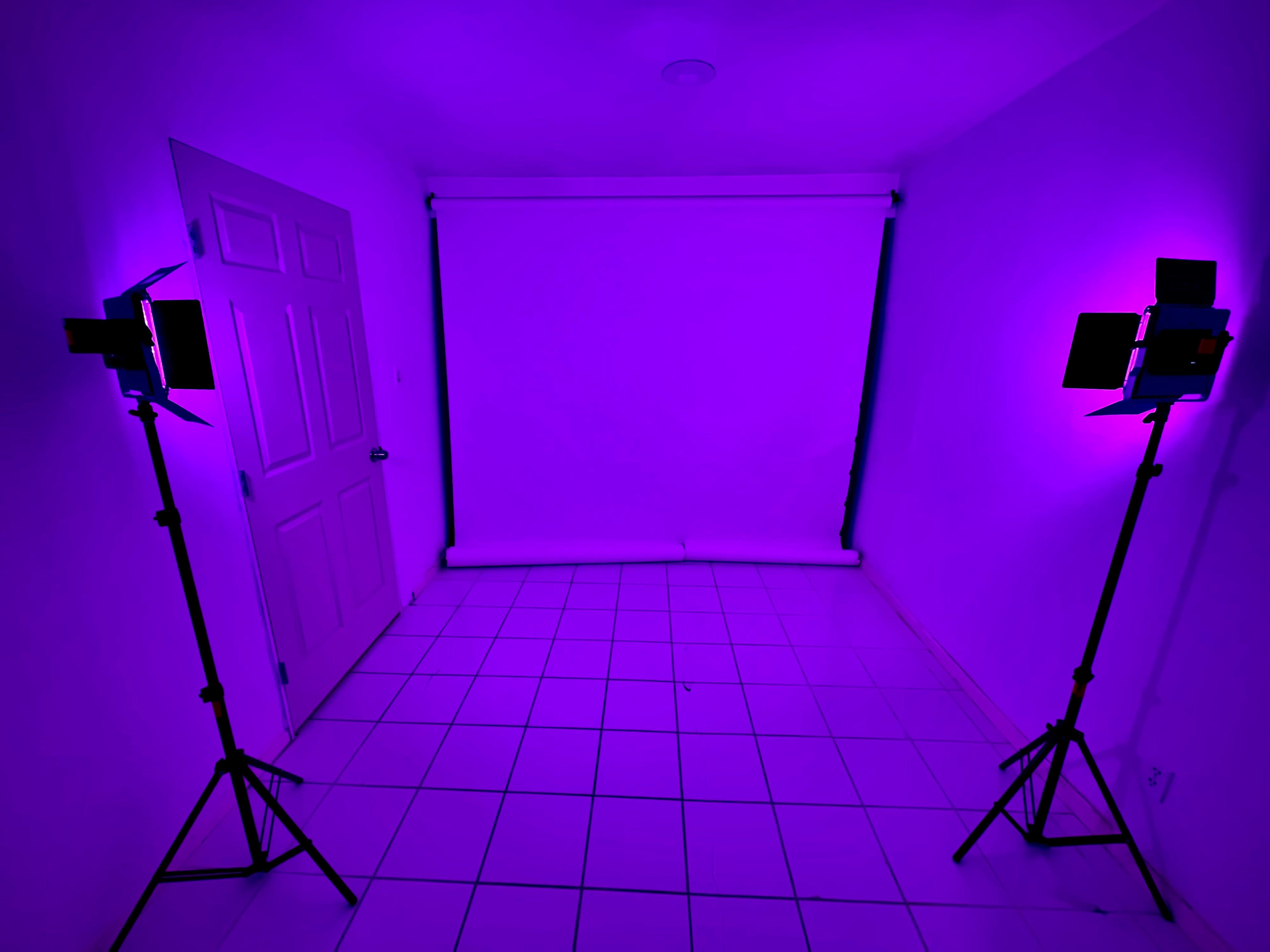 The image shows a sparsely furnished room with two lighting setups positioned on either side of a blank white backdrop.