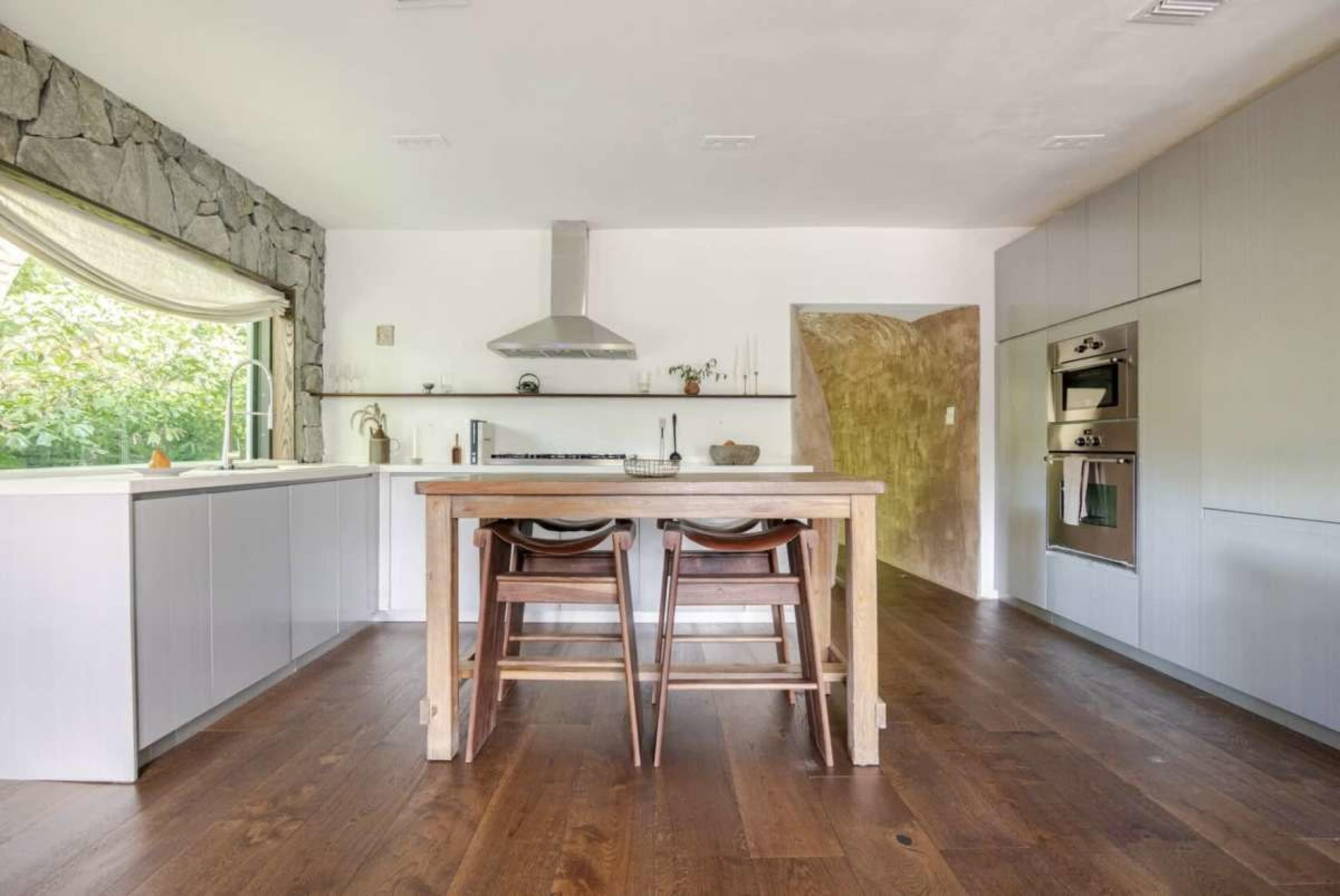 The image shows a modern kitchen with a wooden dining table and four chairs, featuring stone and sleek cabinetry along the walls.