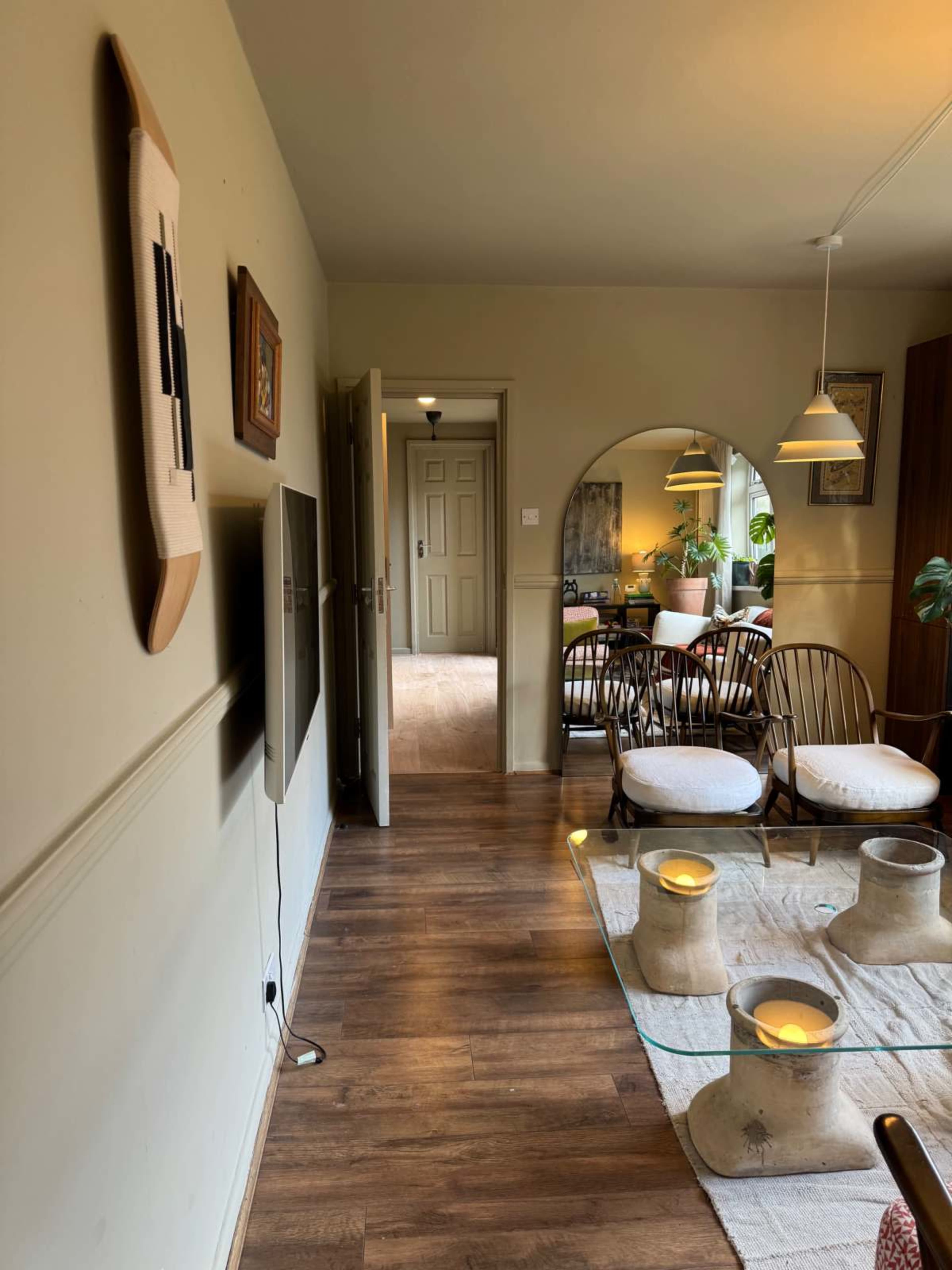 The image shows a cozy interior with a hallway leading to a dining area, featuring a glass coffee table and two chairs in the foreground.
