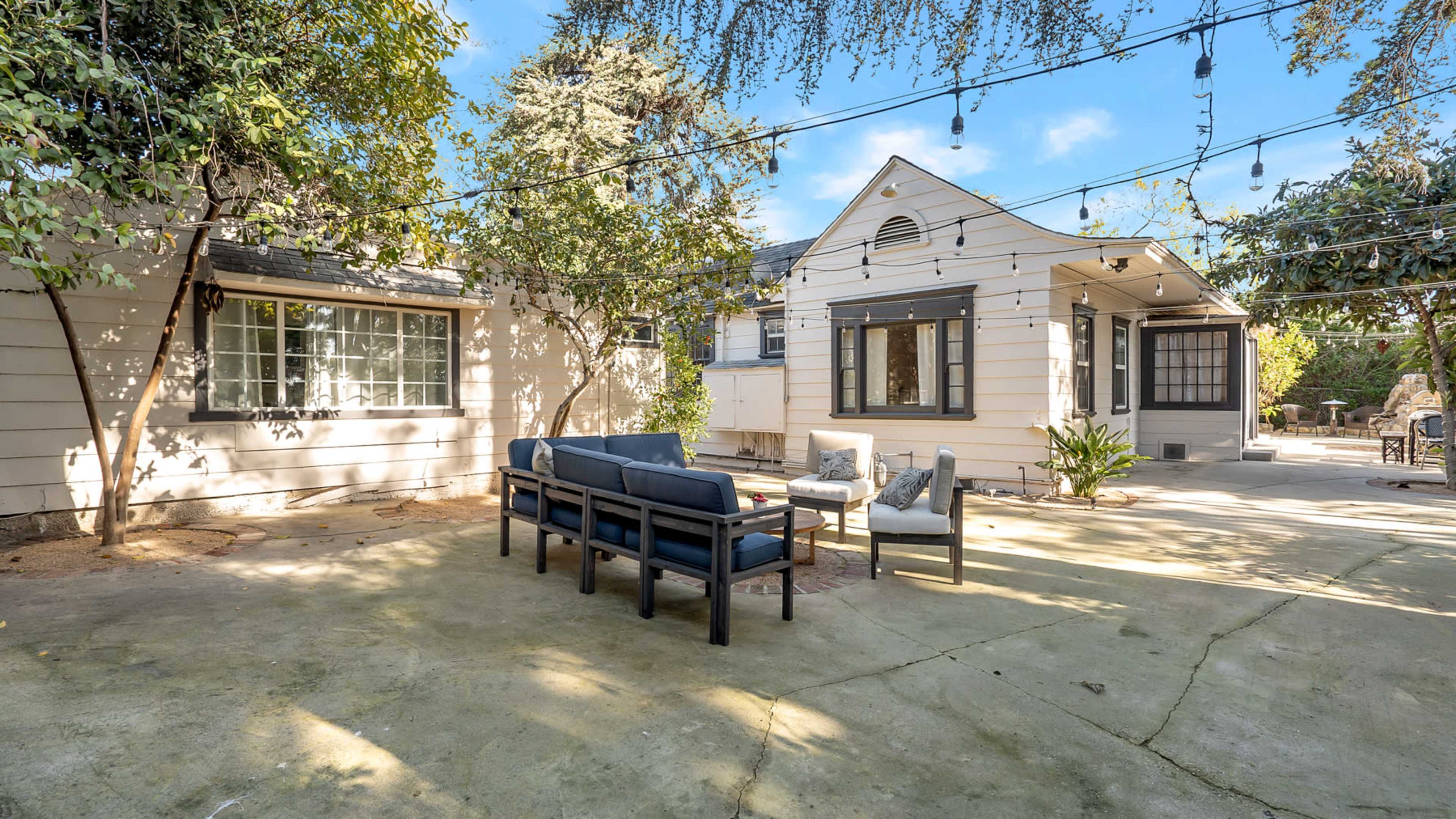 A patio area features outdoor seating and string lights, with a house and garden surrounding it.