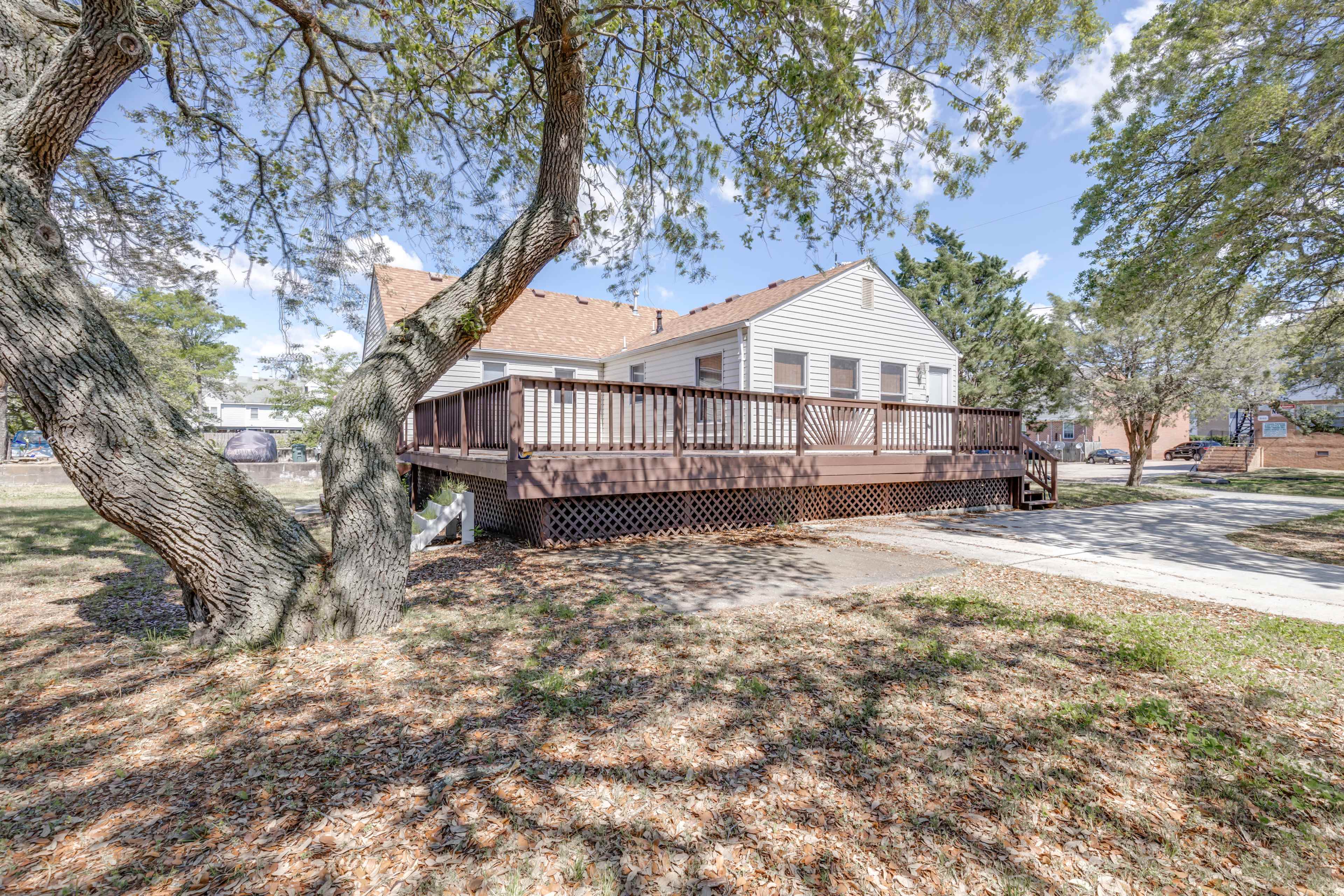 A single-story house with a large wooden deck surrounded by trees and a clear sky.