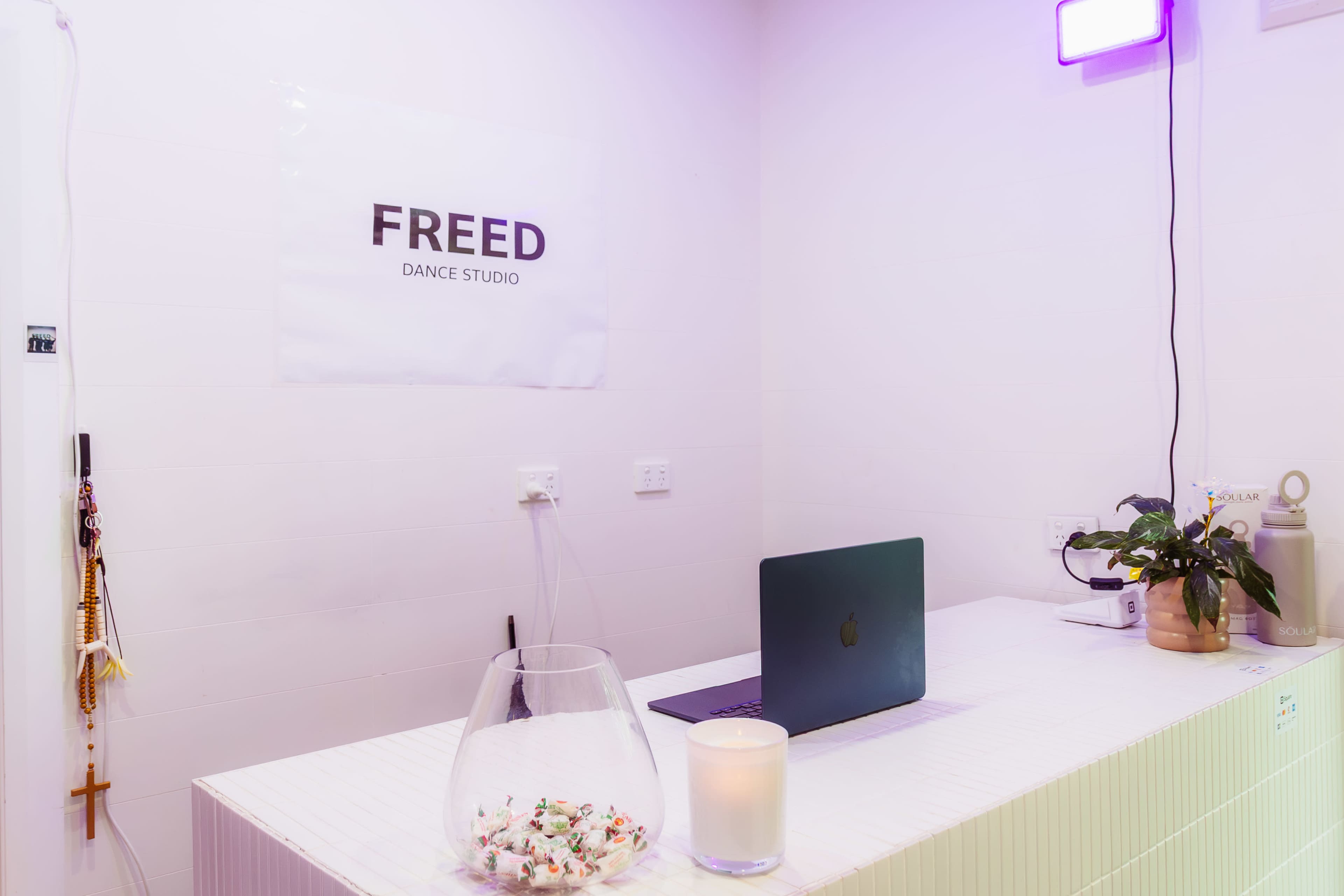 The image shows a reception area of a dance studio with a laptop on a countertop, a candle, and a sign that reads "FREED DANCE STUDIO."