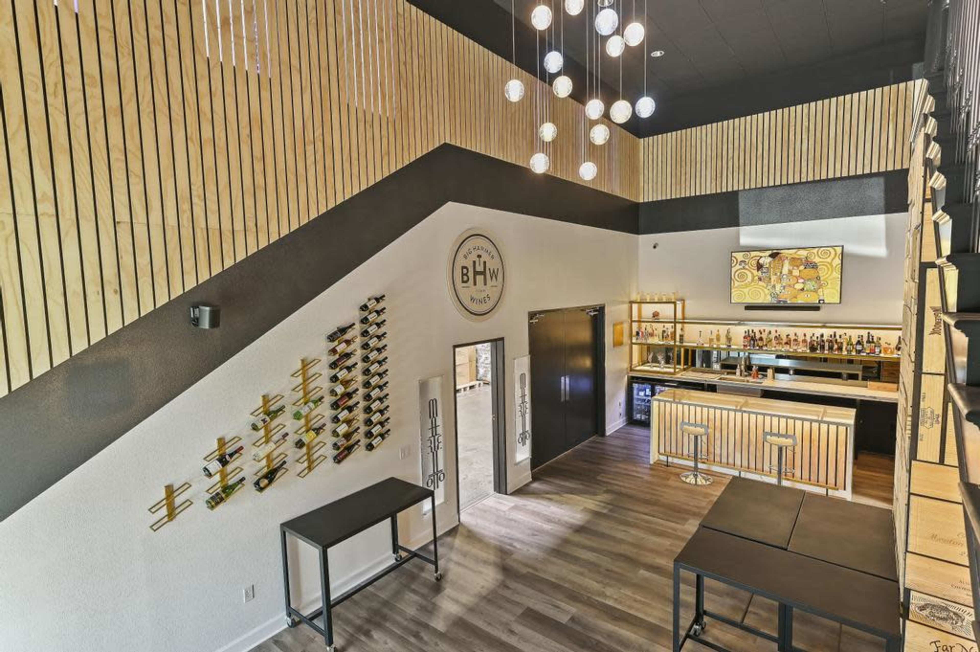 A modern interior of a bar or lounge with wooden paneling, a staircase, and a well-stocked bar counter at the back.