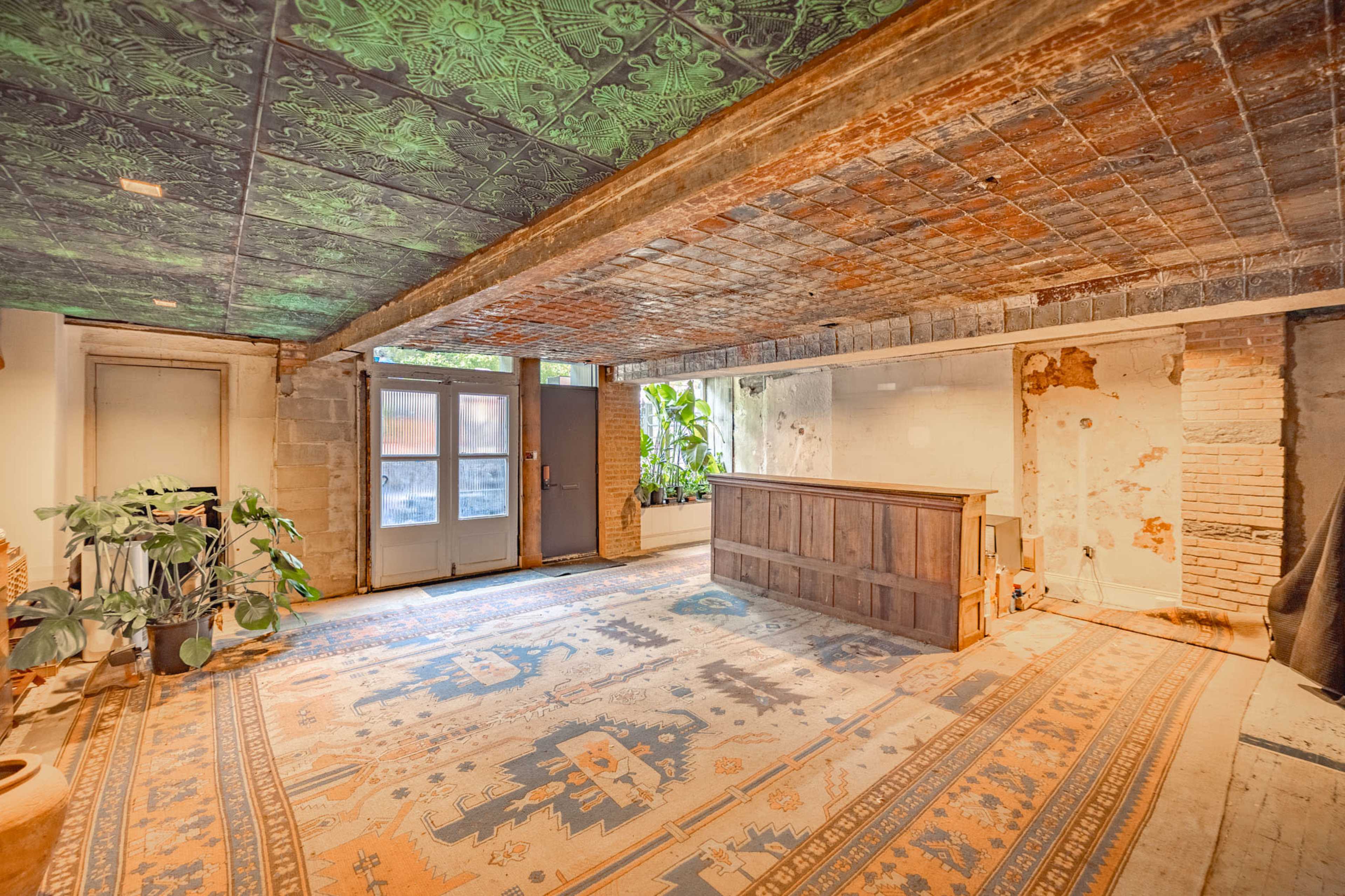 An empty room with a wooden reception desk, patterned rug, and a ceiling featuring ornate tiles.