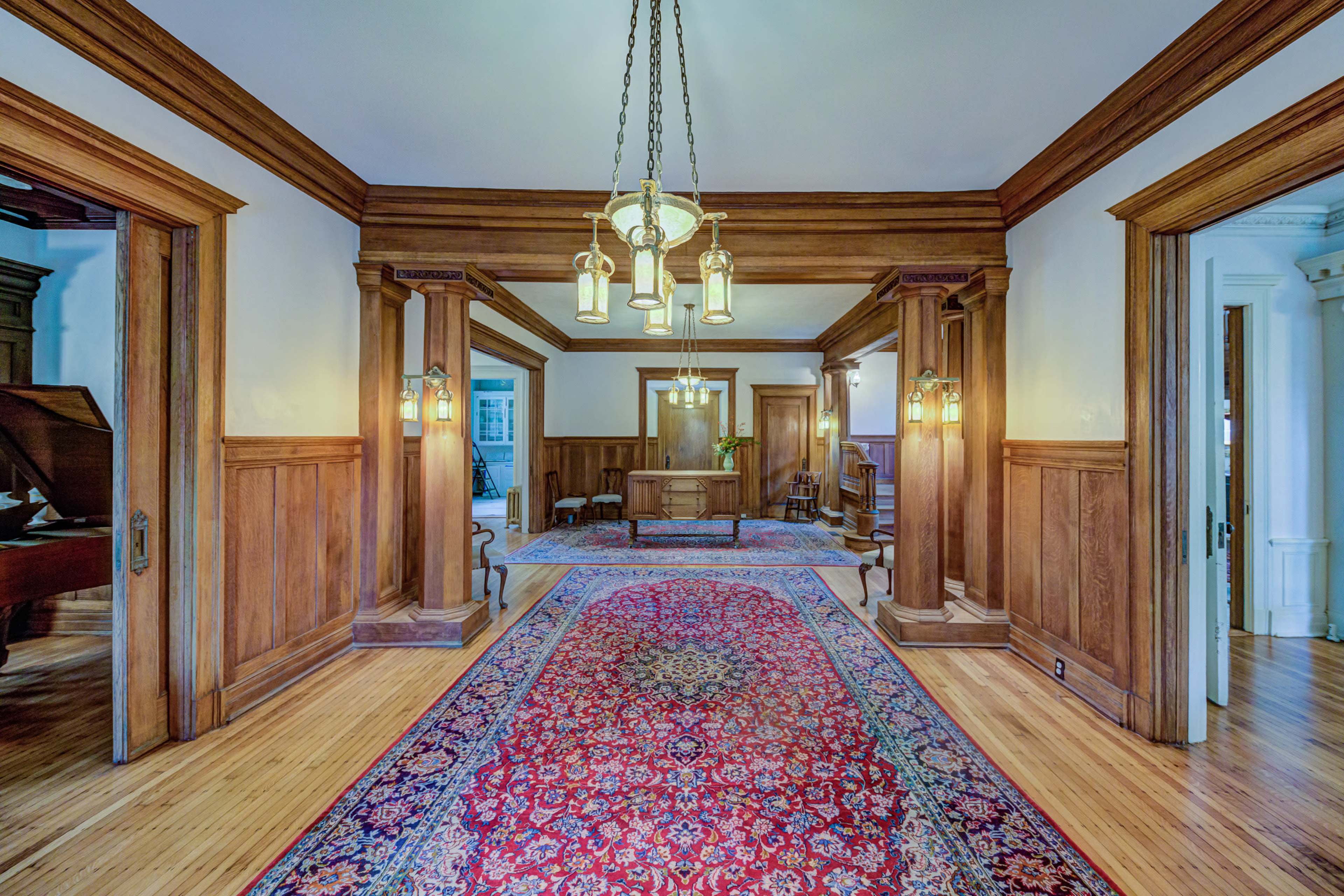A spacious foyer with wooden paneling, a decorative rug, and hanging light fixtures.