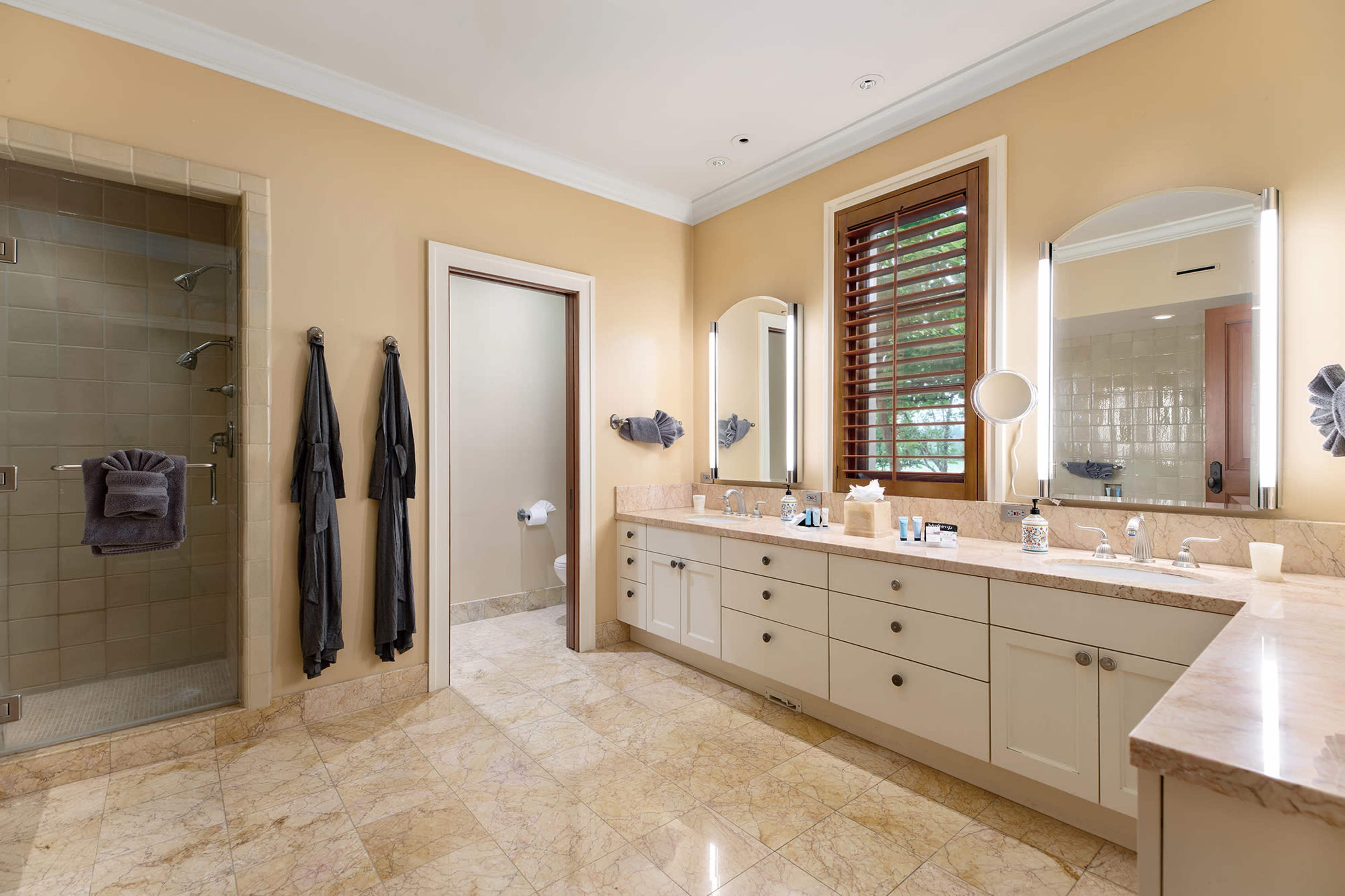 A spacious bathroom featuring dual sinks, a walk-in shower, and two large mirrors, set against beige walls and marble flooring.