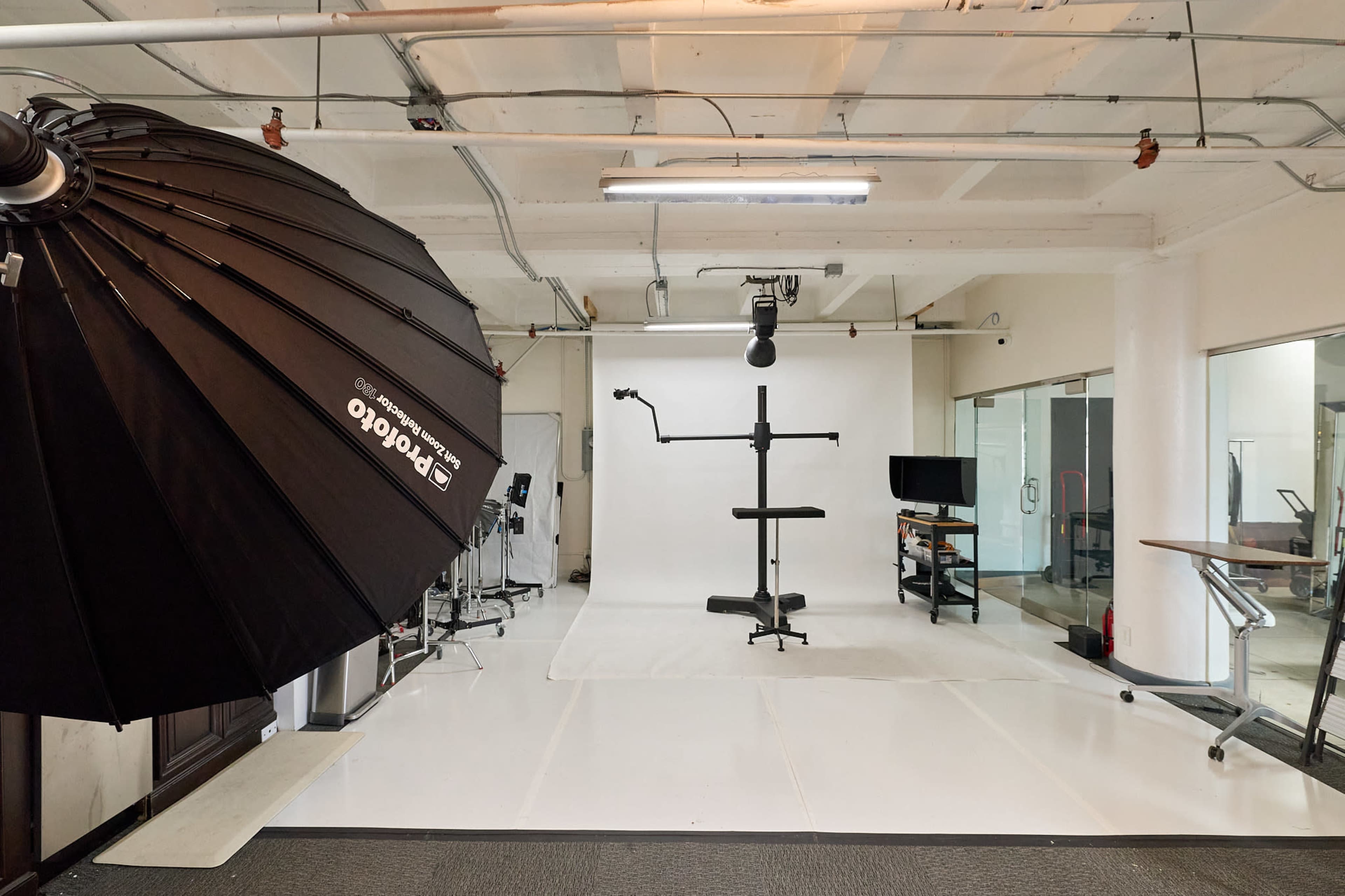 The image shows a photography studio featuring a large softbox light, a backdrop stand, and various pieces of equipment set up in a bright, open space.