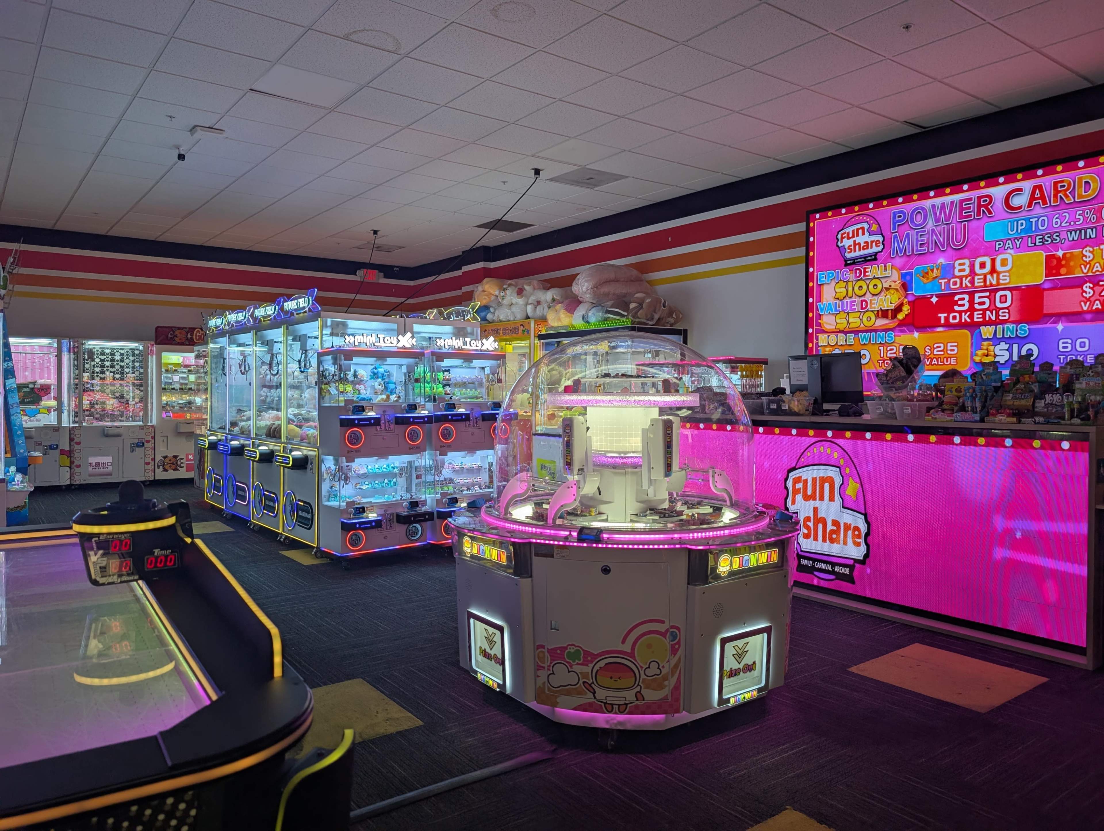 The image shows an indoor amusement arcade featuring various game machines, brightly lit displays, and a prize redemption counter.