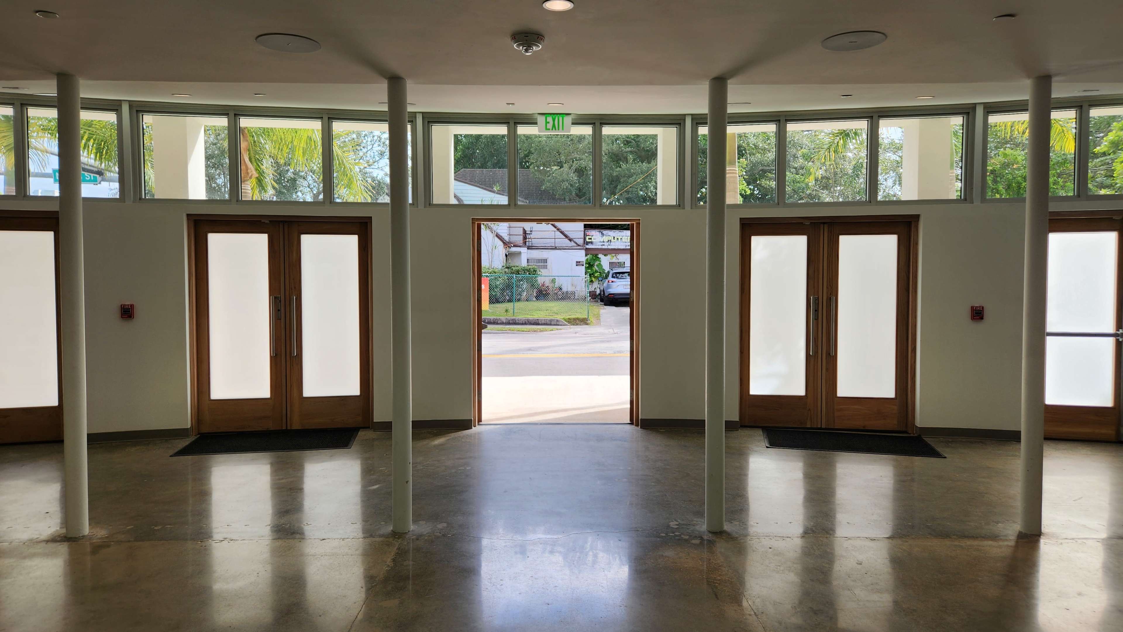 The image shows a modern entrance area with large glass doors on either side, leading to an open outdoor space.