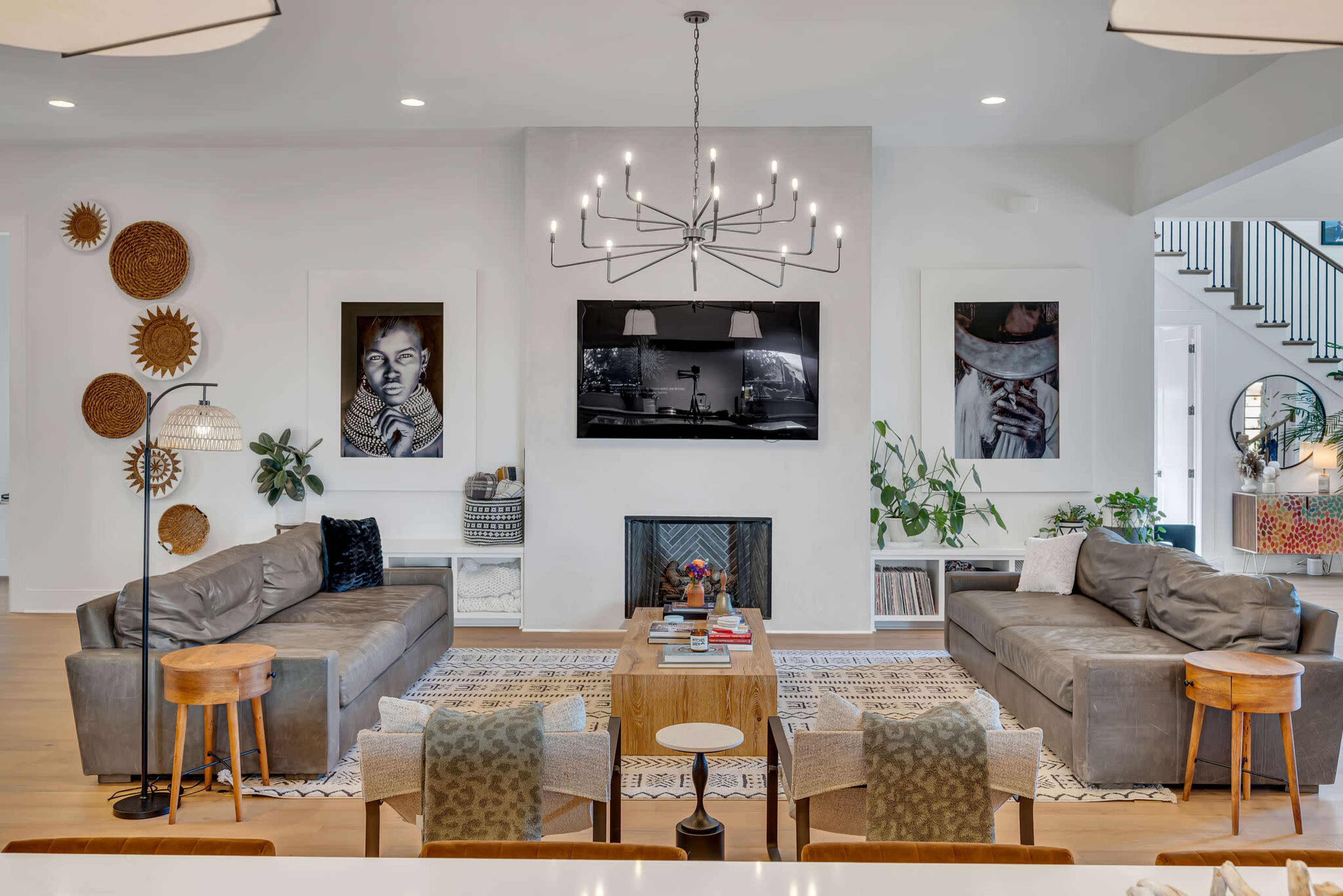 A modern living room features two gray sofas facing a television mounted above a fireplace, surrounded by framed artwork and decorative wall pieces.