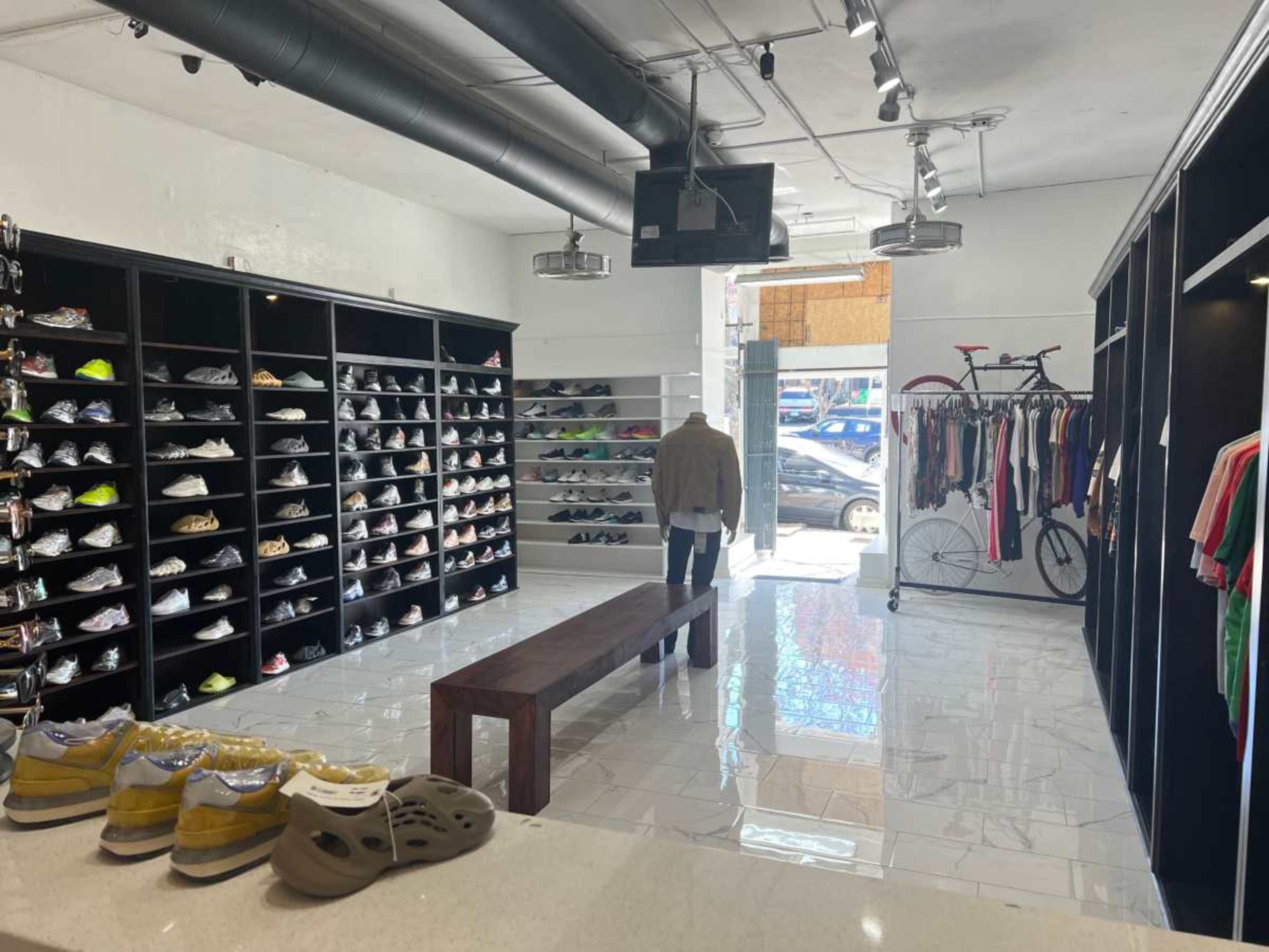 A person walks through a sneaker store featuring a wall of shoes on shelves and racks displaying clothing.