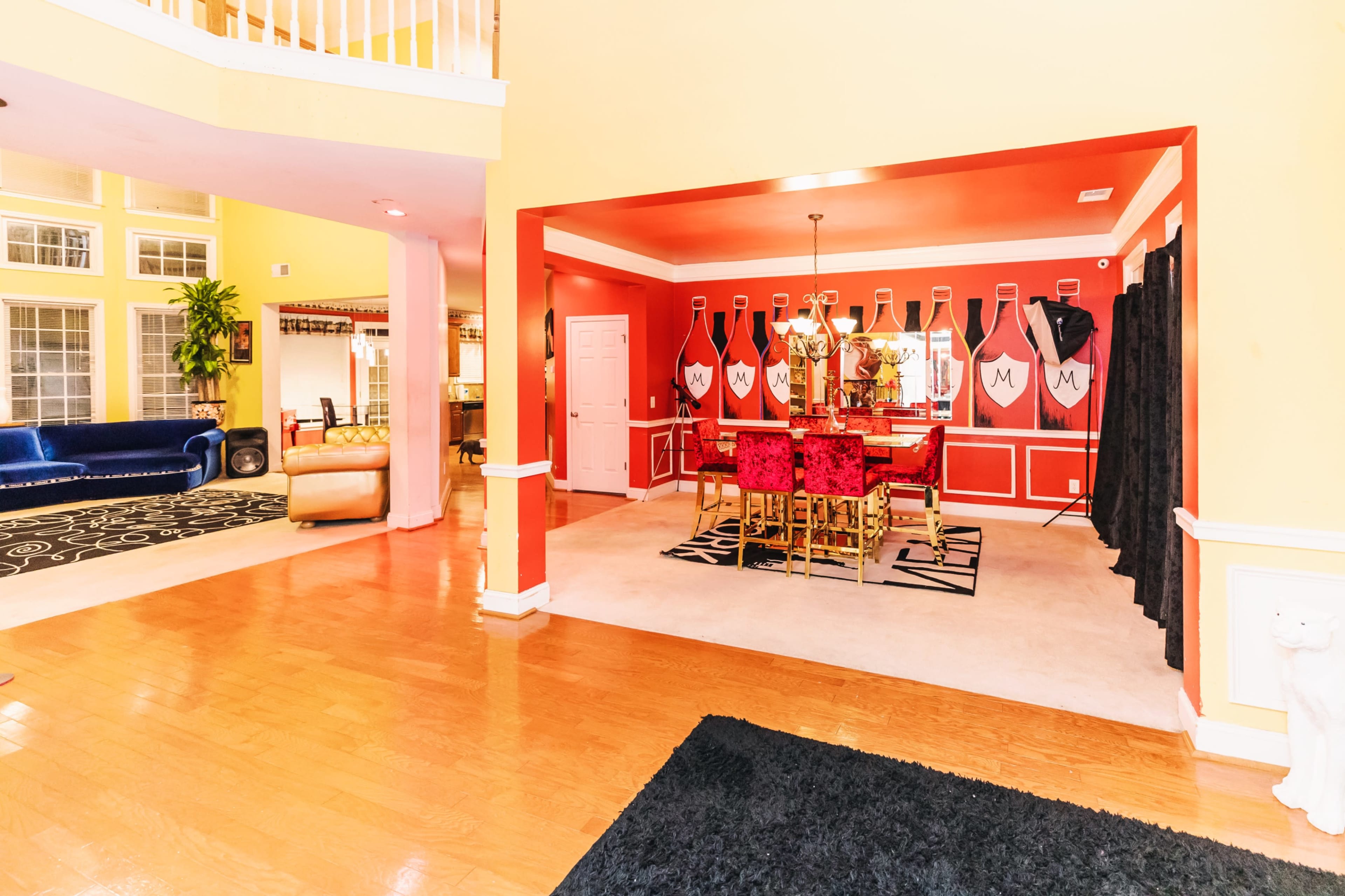 The image shows a spacious open-concept living area with a dining room featuring red decor and a nearby seating area with a blue couch and beige chairs.
