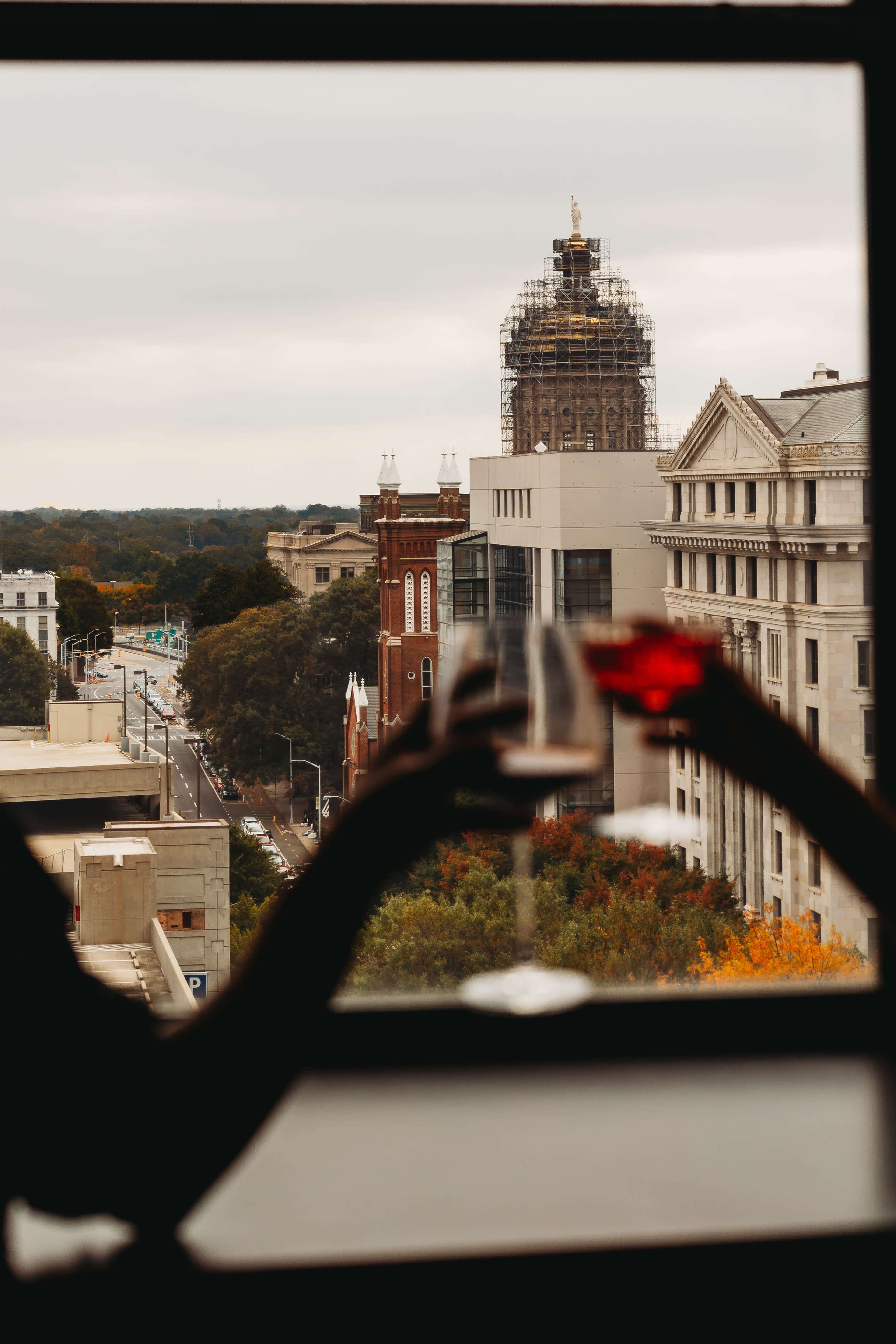 Two glasses are raised in a toast against a backdrop of a city skyline with buildings and a tower under scaffolding.