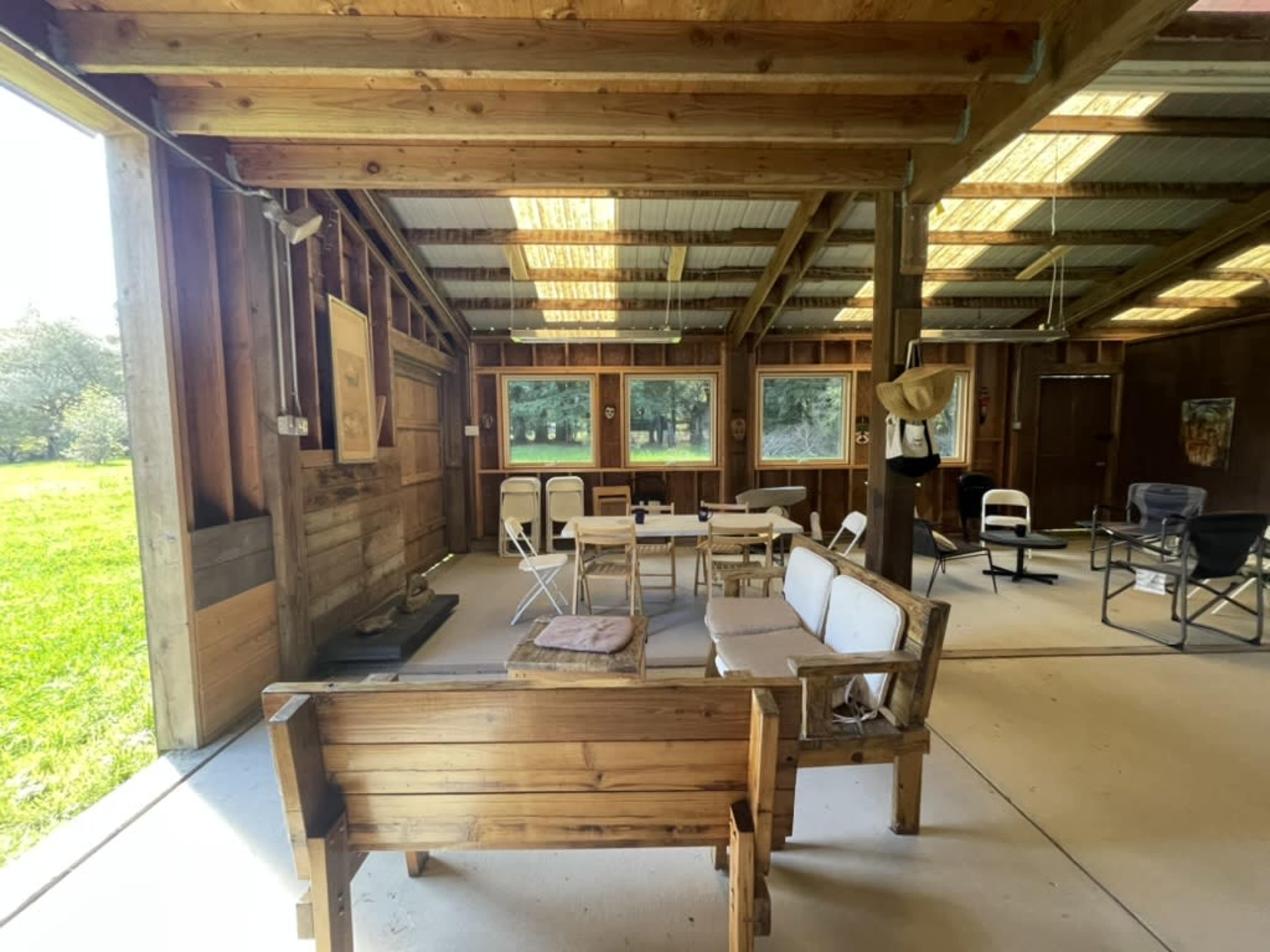 The image shows an indoor space with wooden walls and a concrete floor, featuring several chairs and tables arranged for seating.