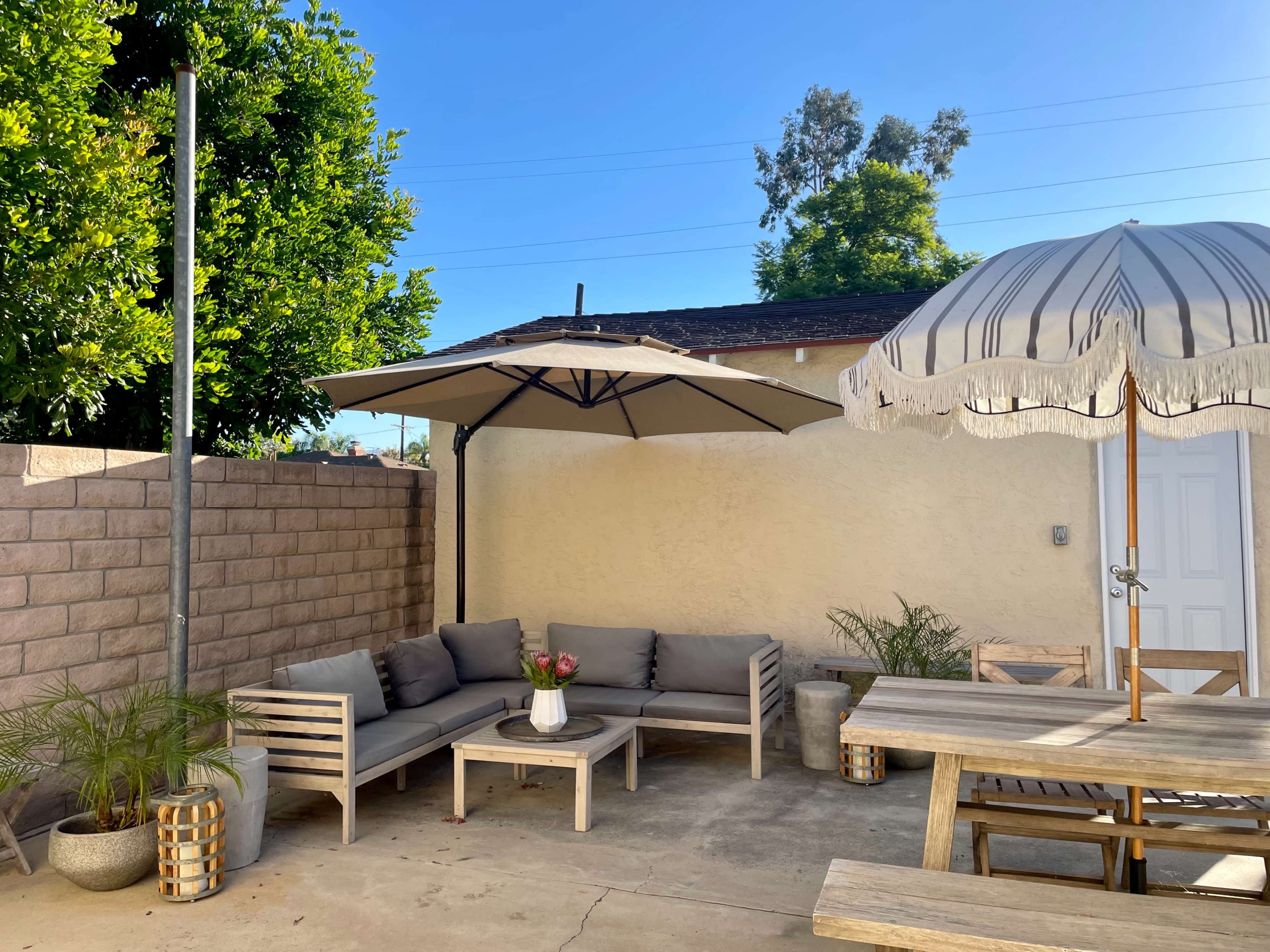 A patio area features a gray sectional couch, a table with a flower vase, and two umbrellas for shade.