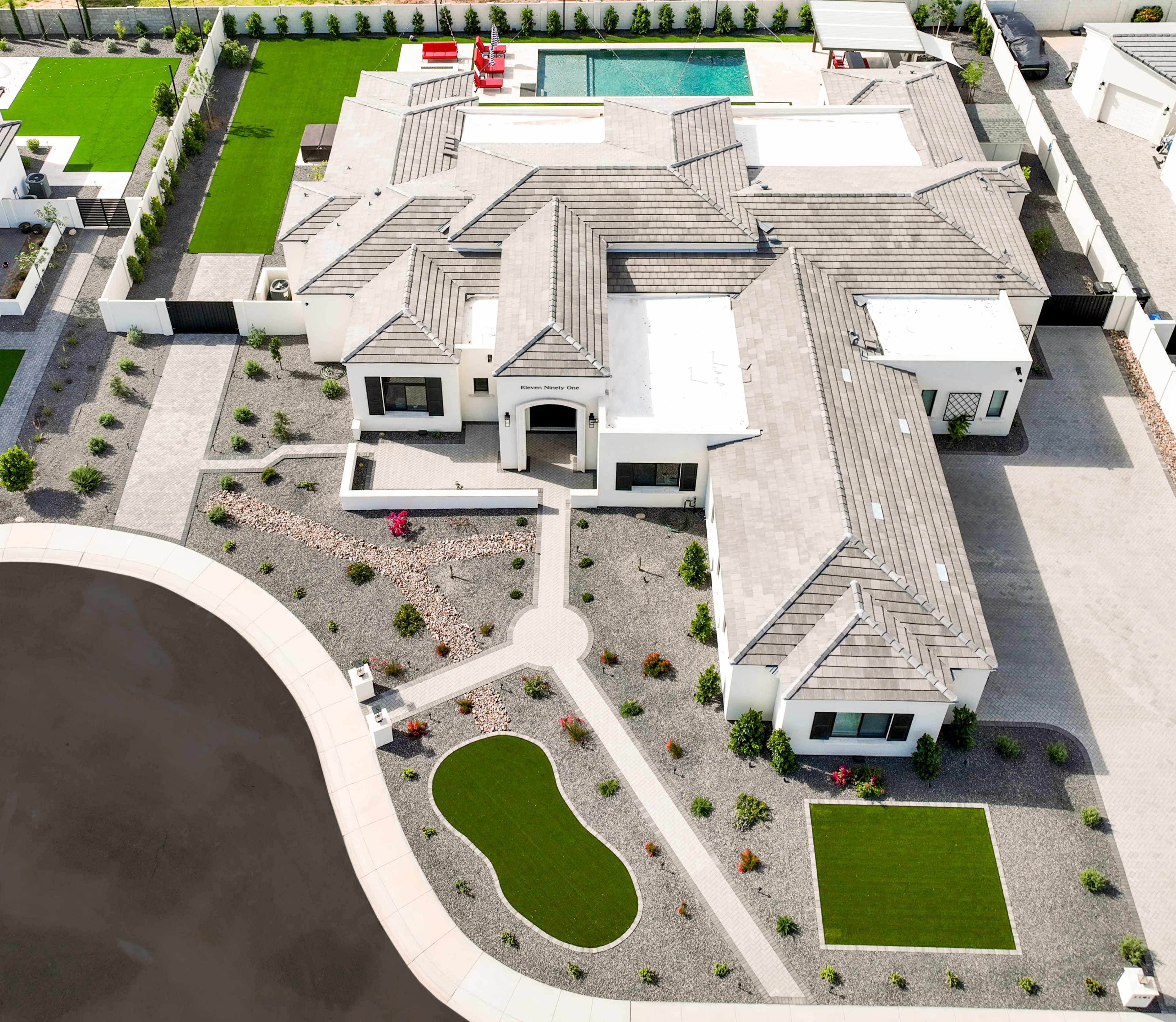 An aerial view of a large modern house with a landscaped yard, a swimming pool, and curved pathways.