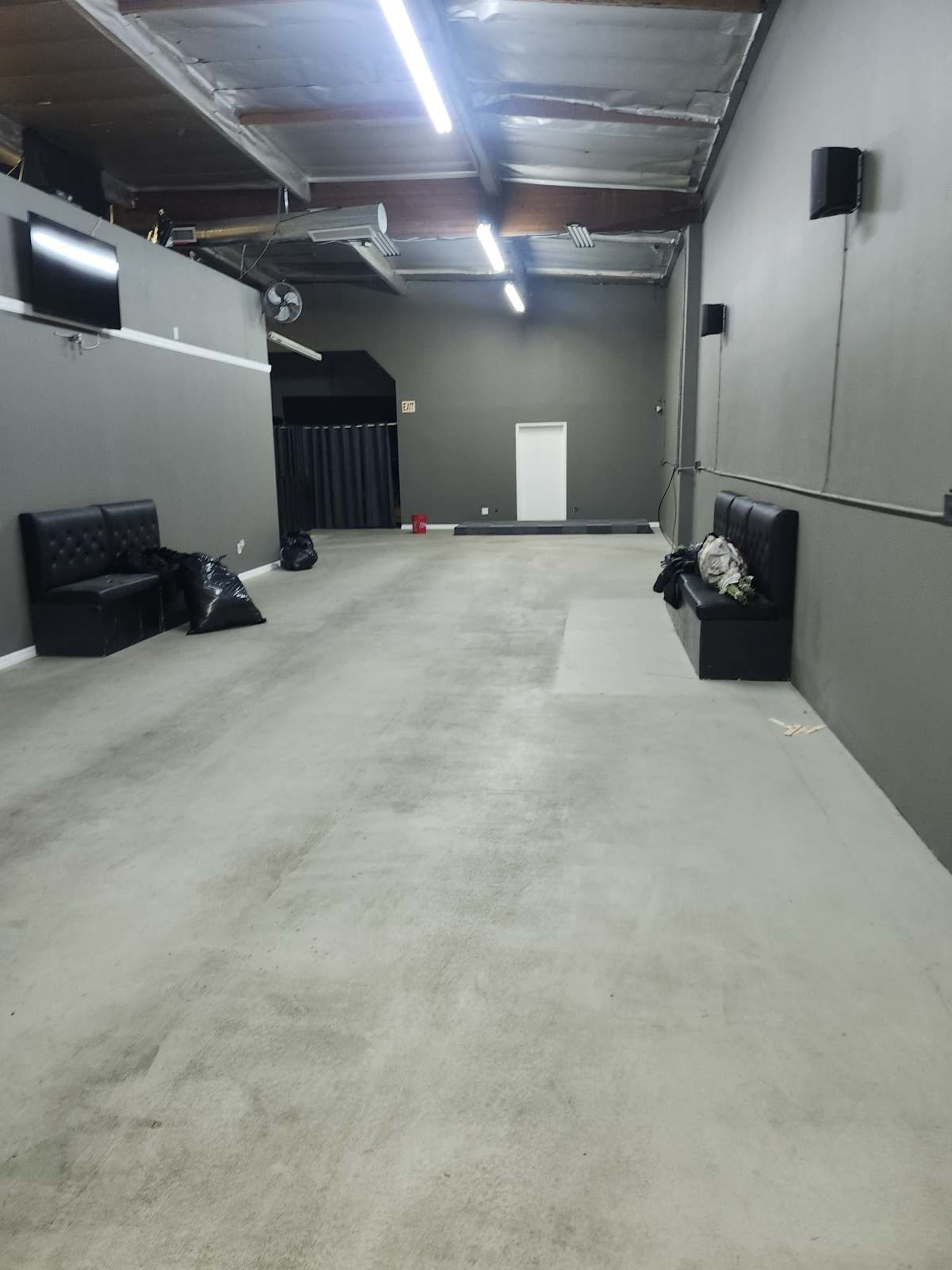 The image shows a spacious, empty room with gray walls, concrete flooring, and two black benches along one side.