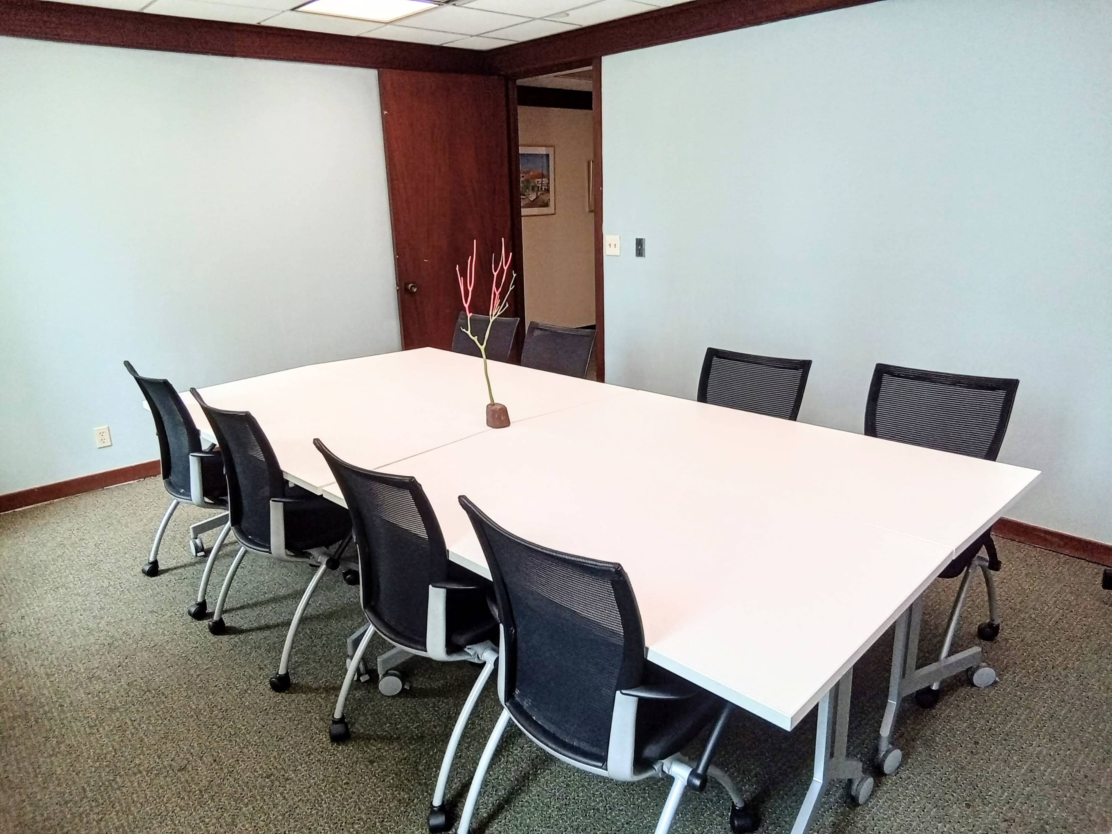 A large, empty conference table surrounded by ergonomic chairs is set in a well-lit meeting room.